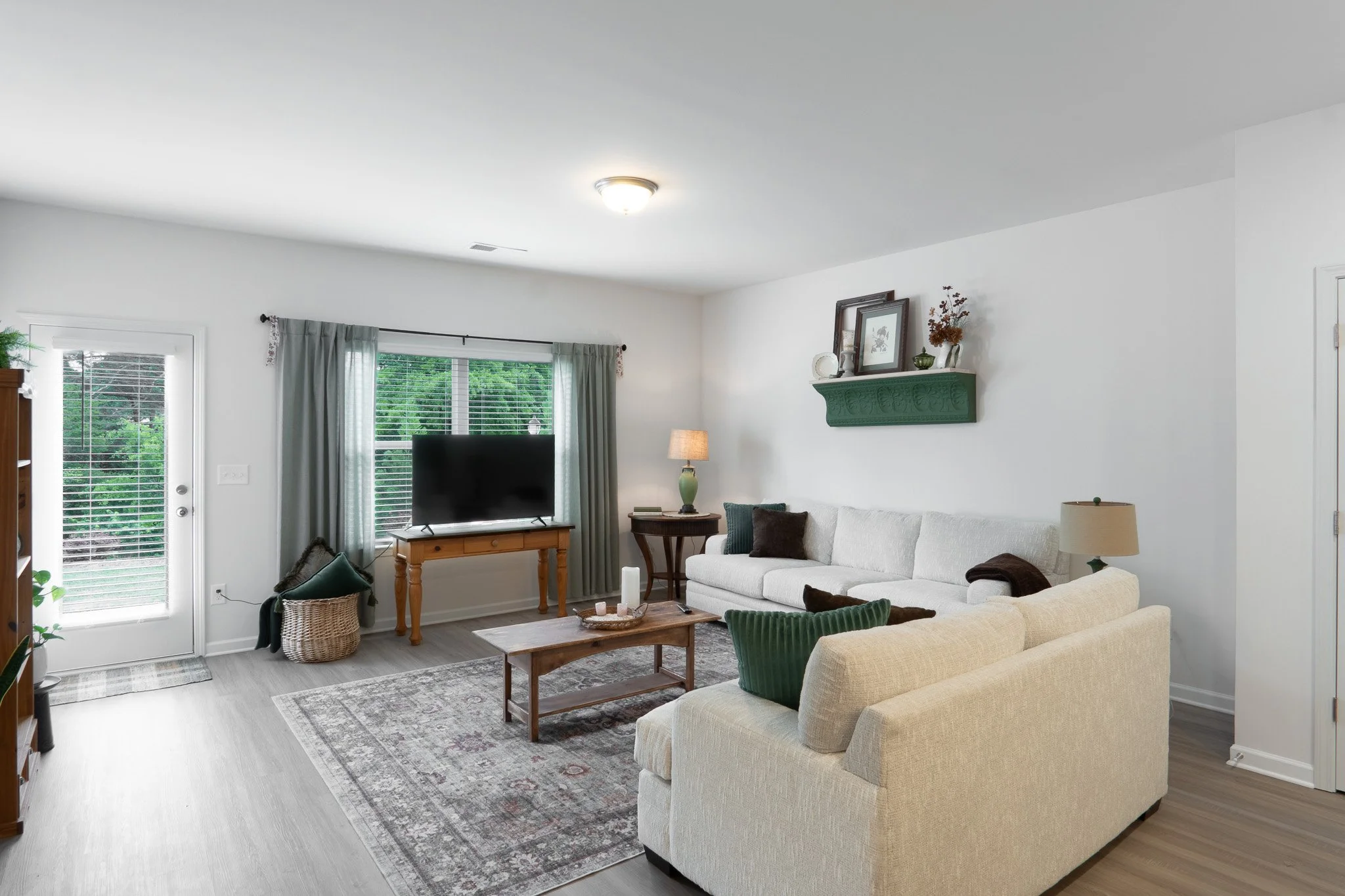 A living room with a beige sofa, a coffee table, a television, and large windows with curtains.