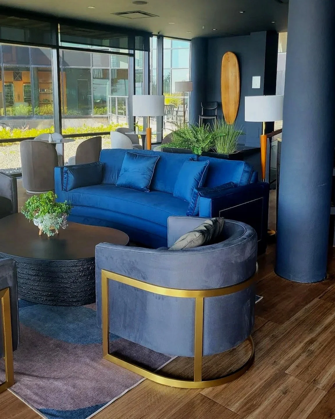 Interior of a modern lounge with a blue velvet sofa, a grey curved armchair with gold trim, a round coffee table with a plant, multiple white and grey chairs. Commercial Design from Spirit design studio - Vancouver island interior decorator