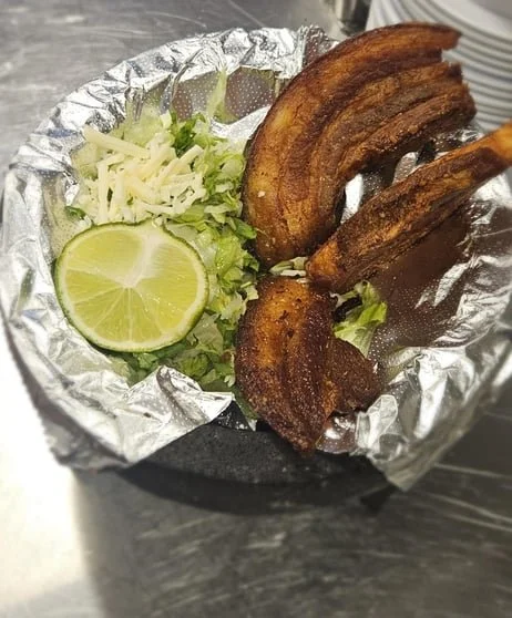 Fried pork belly slices with a wedge of lime and shredded cabbage, served on aluminum foil.