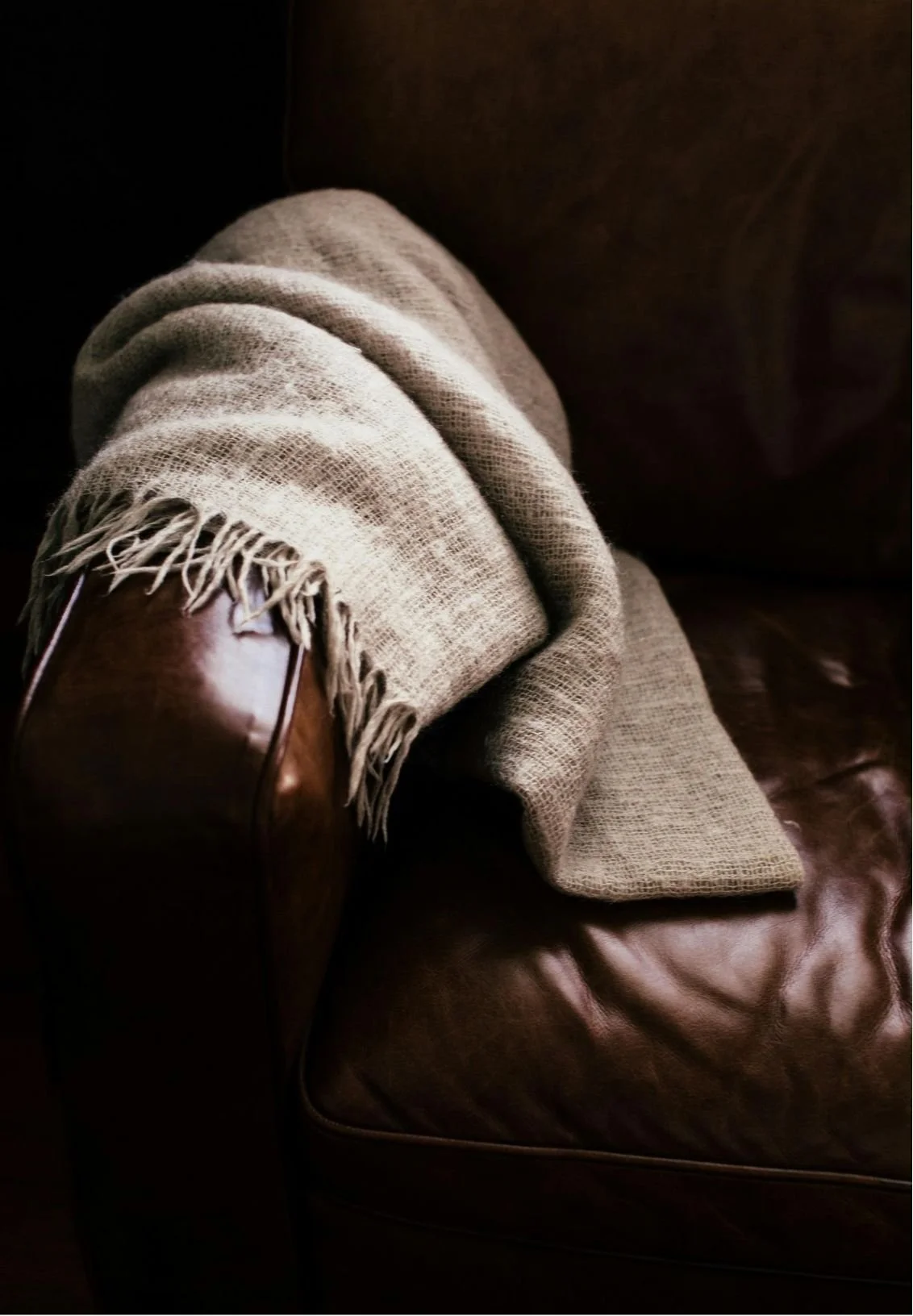 Close-up of a person's legs wearing beige pants and a tan scarf, resting on a brown leather sofa.