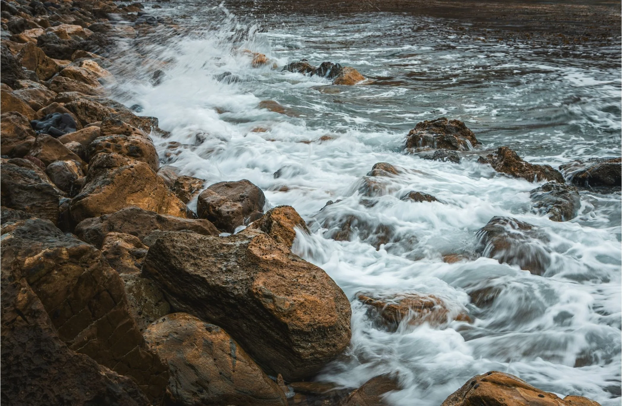 Waves crashing against rocks along the shoreline of a body of water.