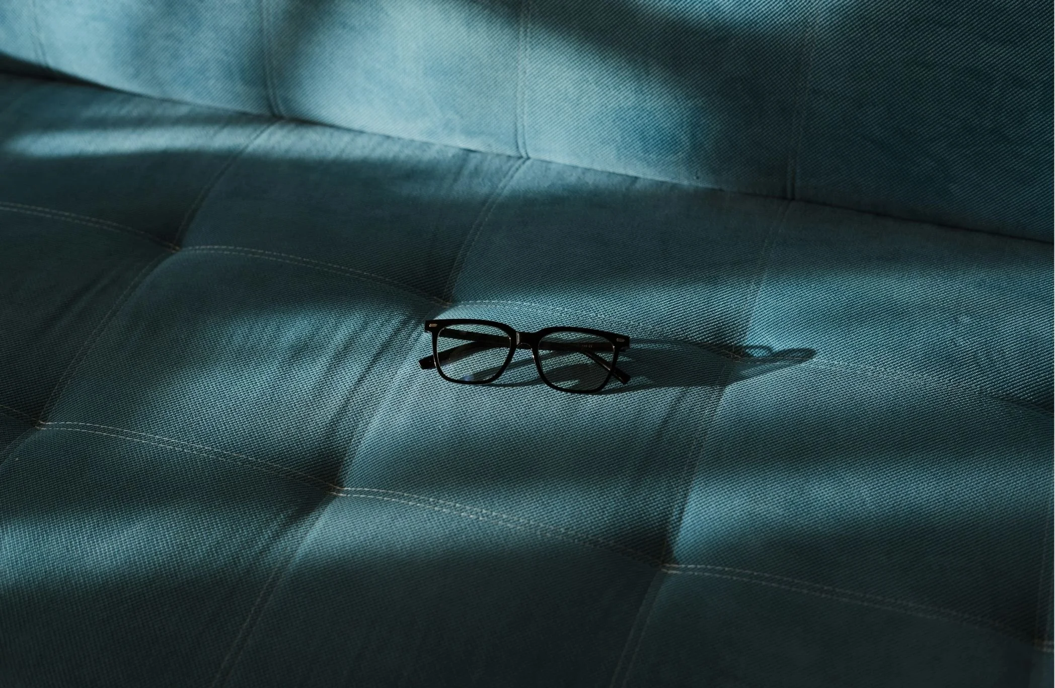 A pair of black eyeglasses resting on a blue textured leather sofa.