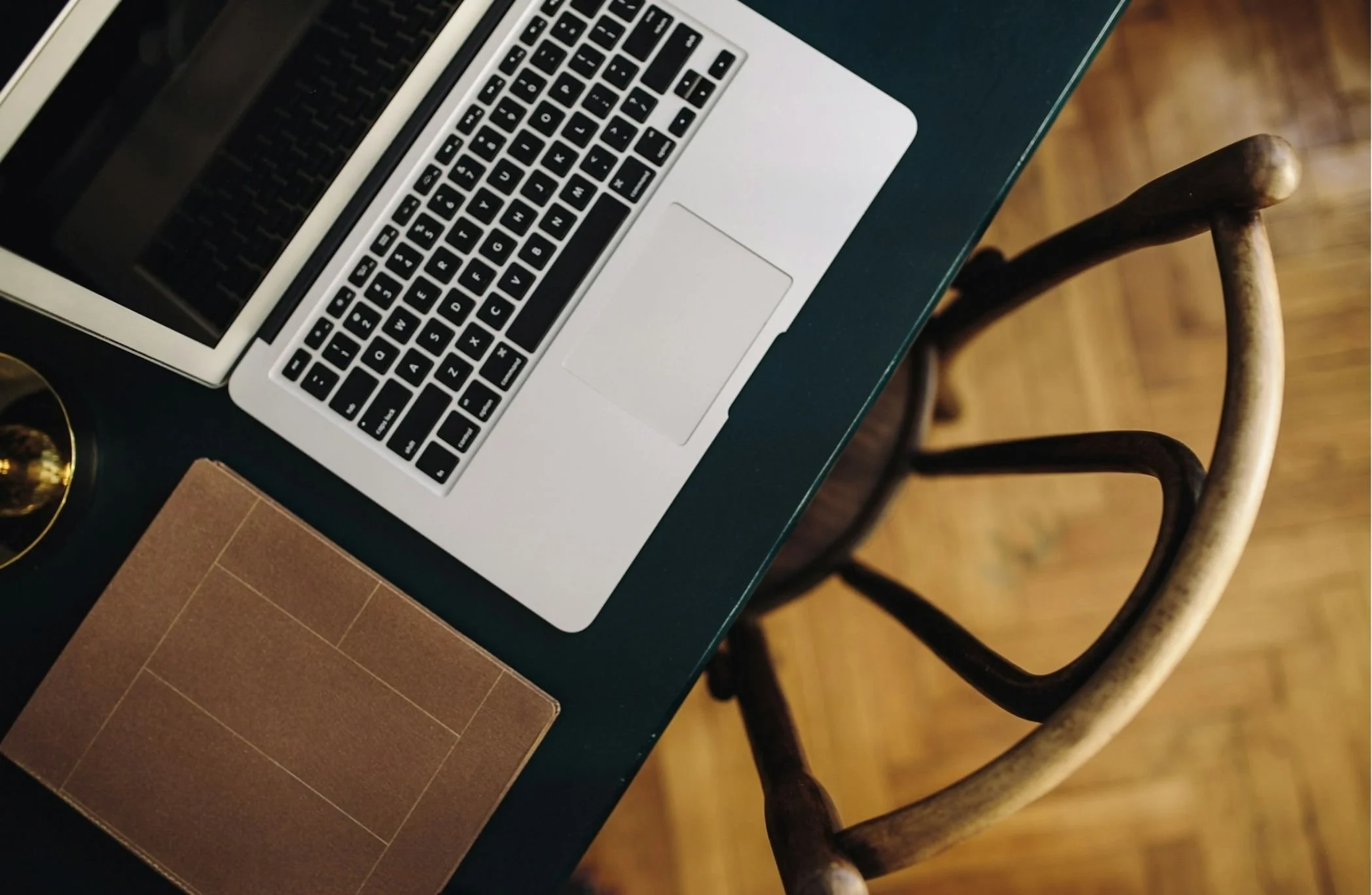 Close-up of a silver laptop with black keyboard on a dark green table, beige chairs, wooden floor.