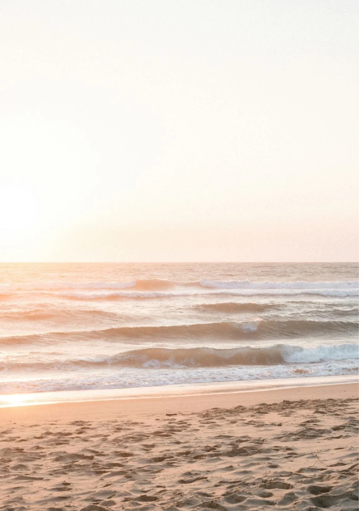 A serene beach scene at sunset with gentle waves, sandy shoreline, and soft pastel sky colors.