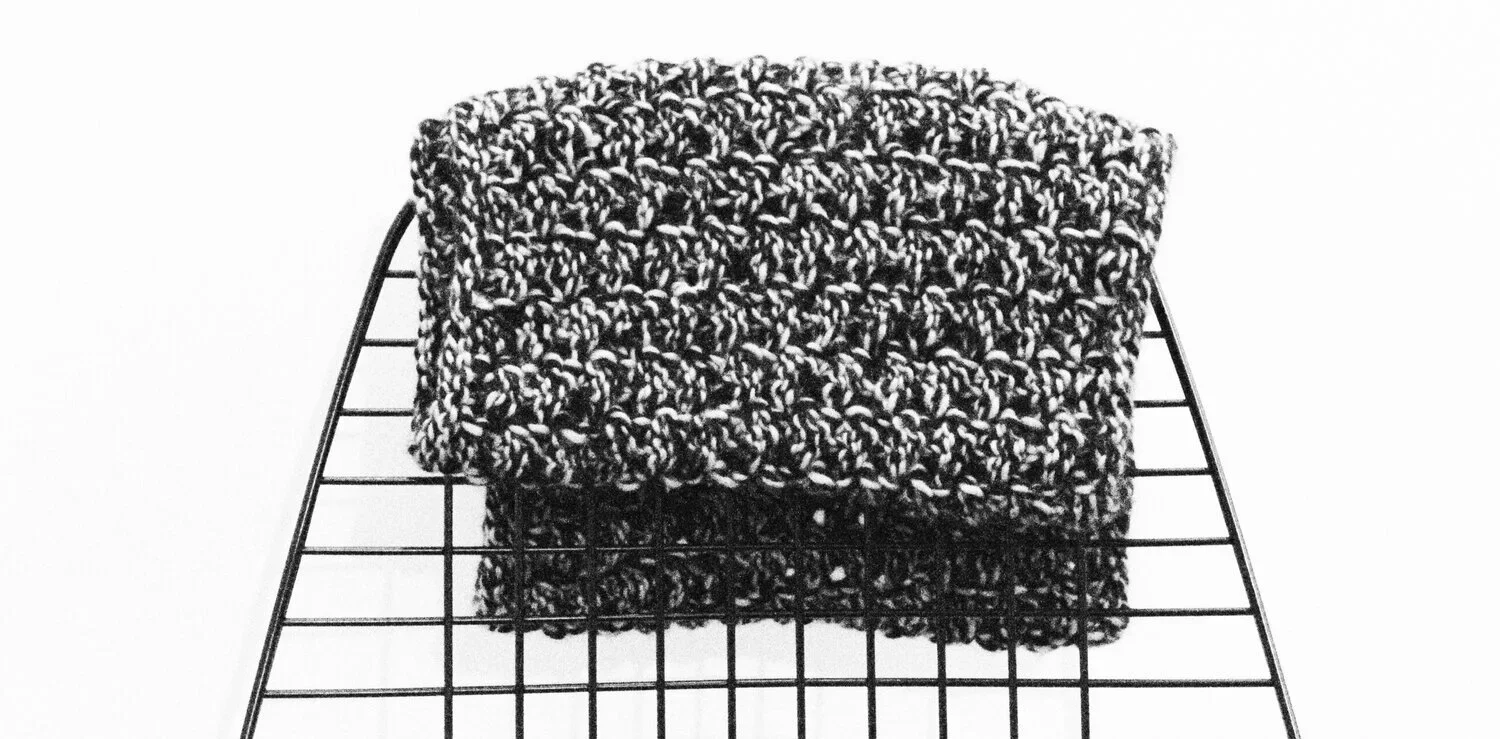 Close-up of chunky hand-knit fabric in black and white yarn displayed on a wire rack