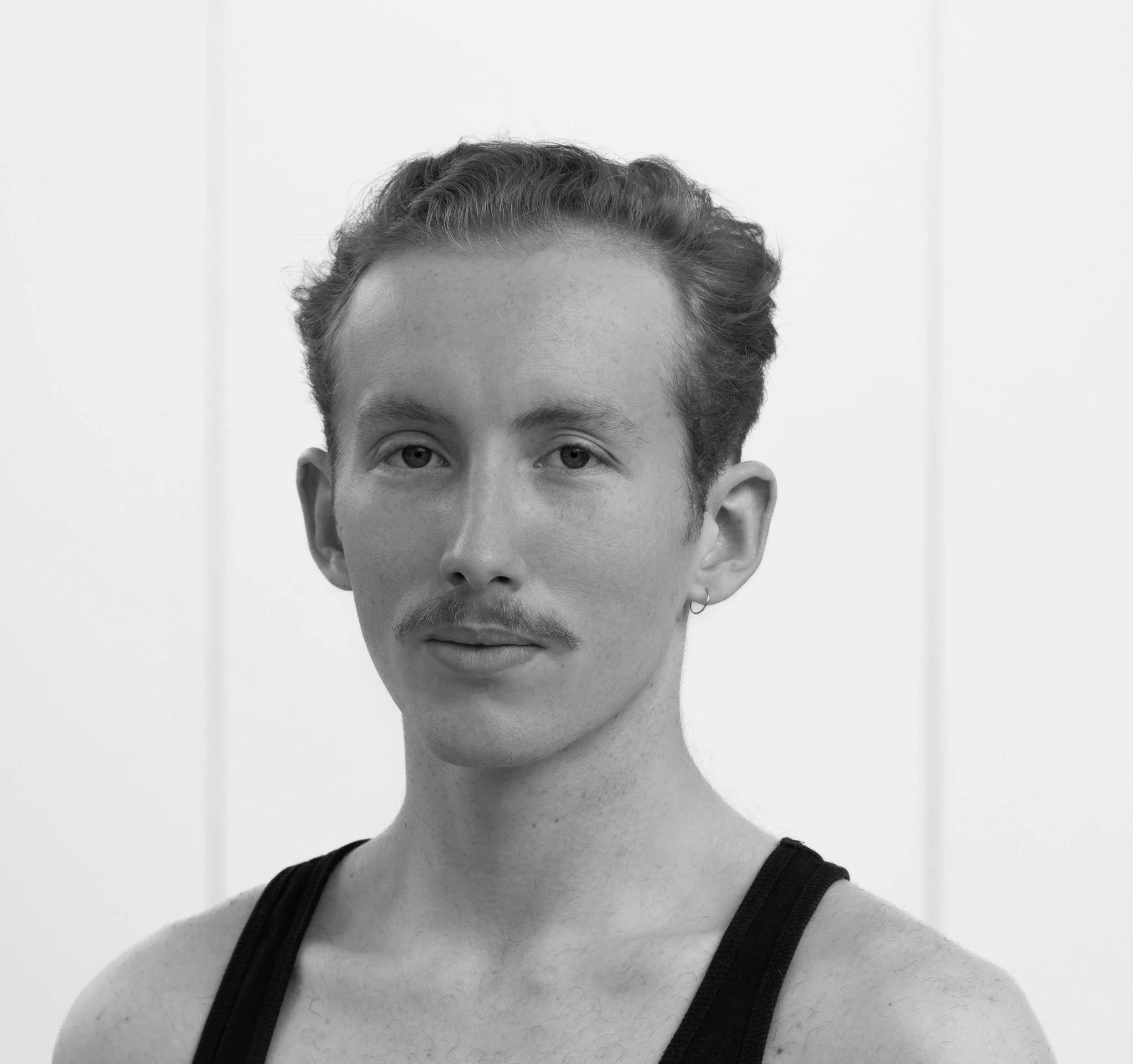 Black-and-white photo of a young person with curly hair, looking directly at the camera, wearing a sleeveless top.