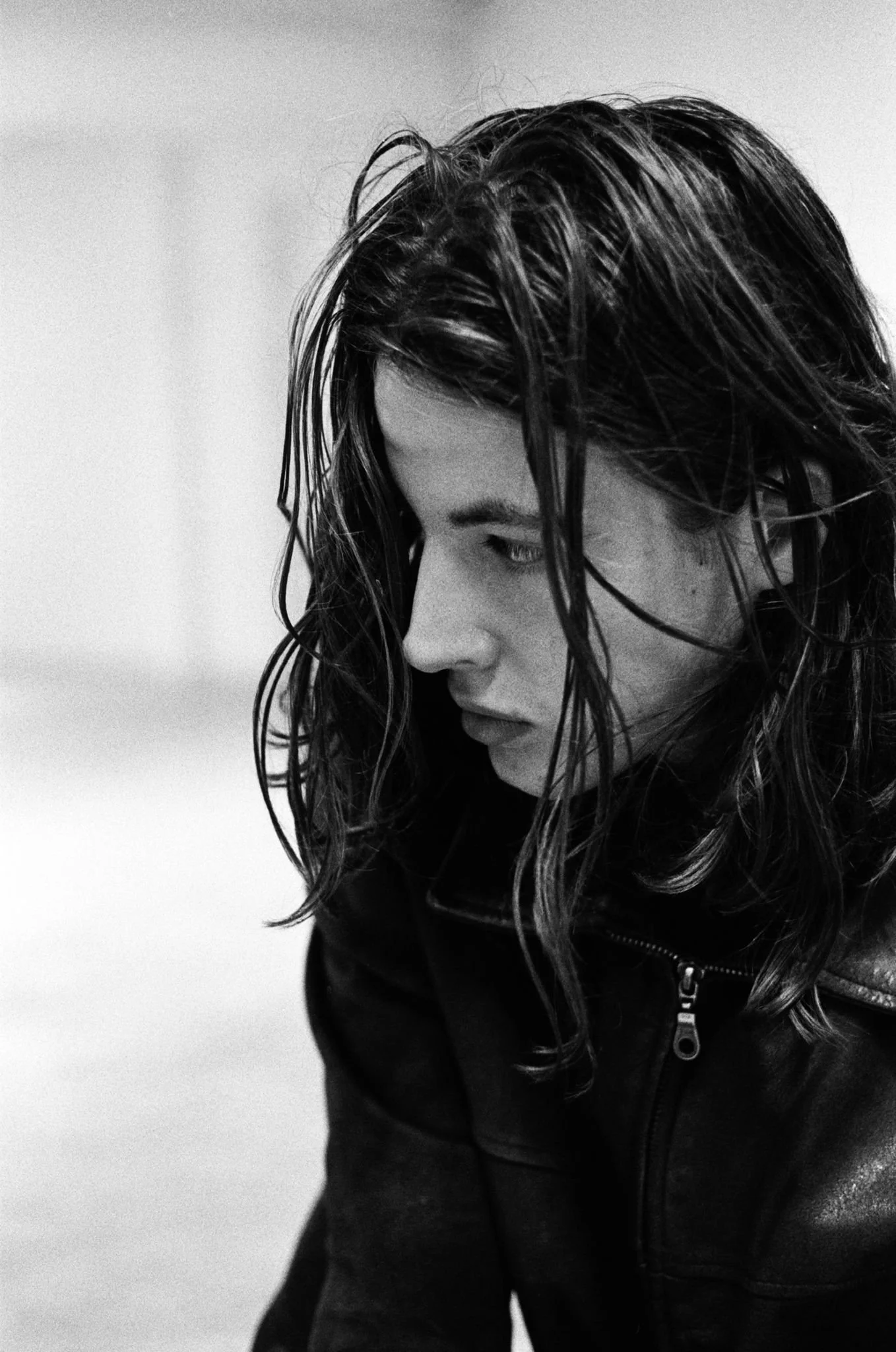 Black and white photo of a woman with wet, messy hair wearing a black leather jacket, looking downward.