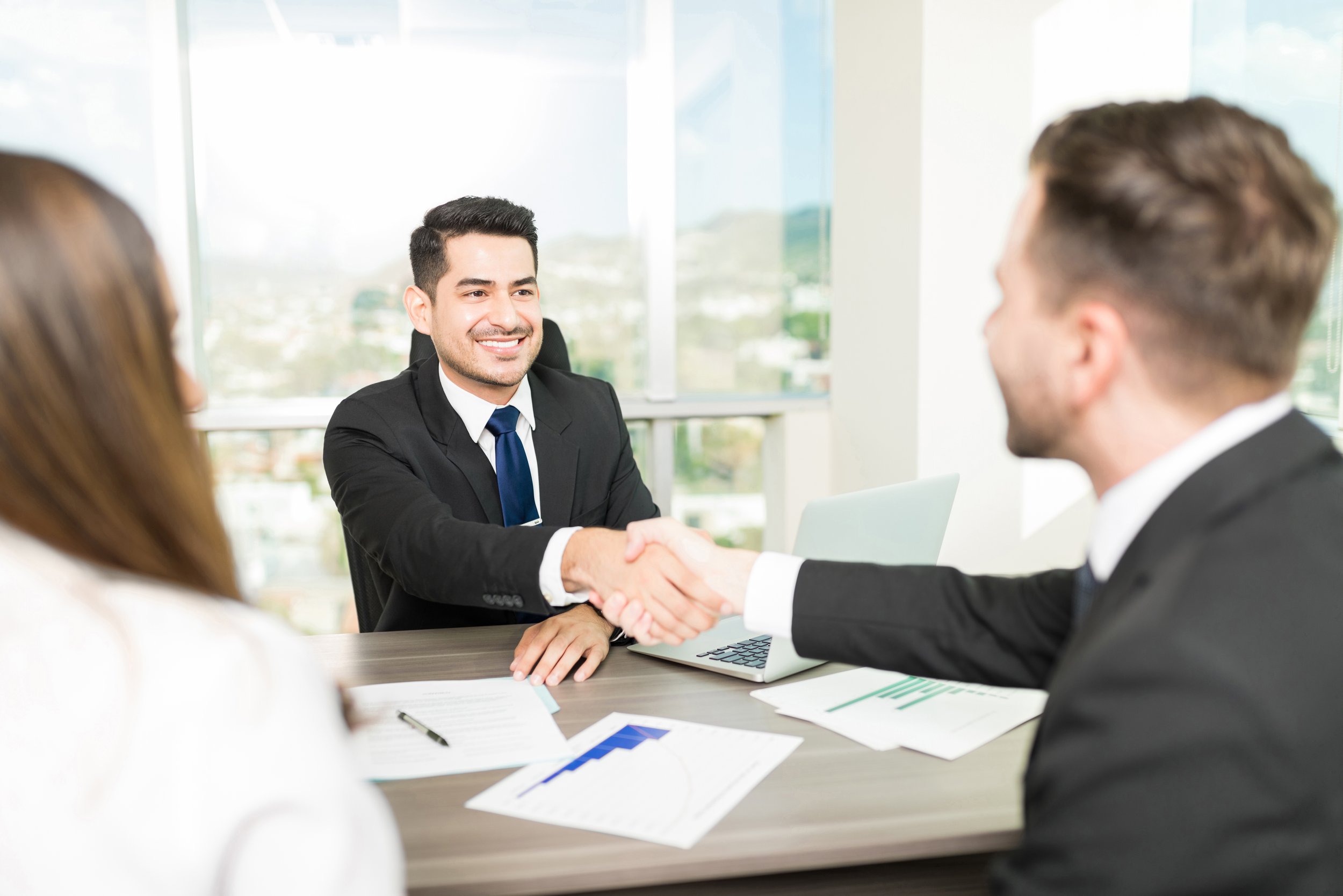 A man in a suit shaking hands with another person in a professional setting during a meeting.
