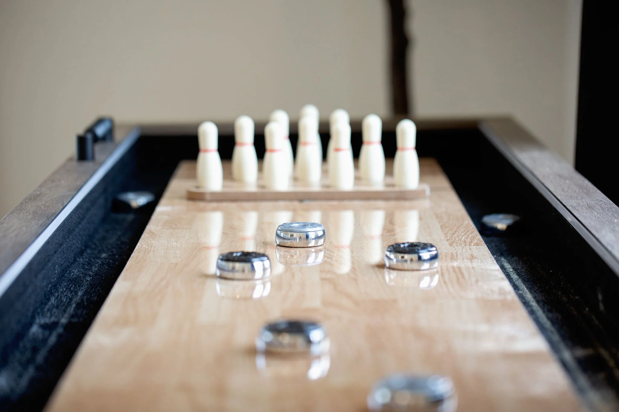 Close-up of a game of shuffleboard, focusing on the puck and pucks lined up at the end of the court with wooden surface and black edging.