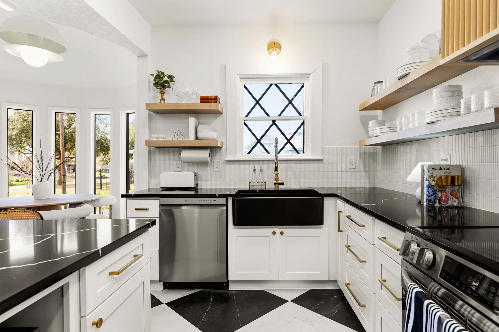 Modern white kitchen with black countertops, open shelves, and a window with black crossbars, decorated with dishes and glassware.