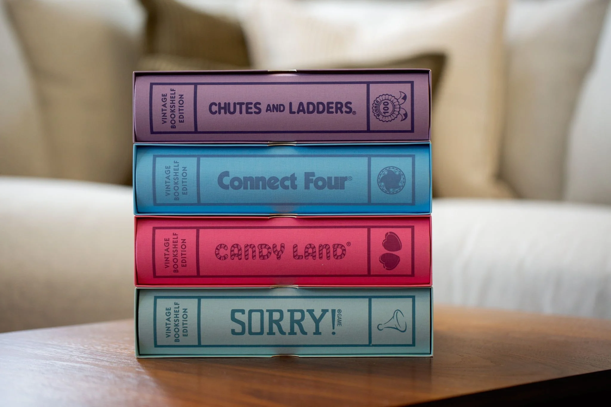 Stacked card games with colorful boxes labeled 'Chutes and Ladders,' 'Connect Four,' 'Candy Land,' and 'Sorry!' on a wooden table.
