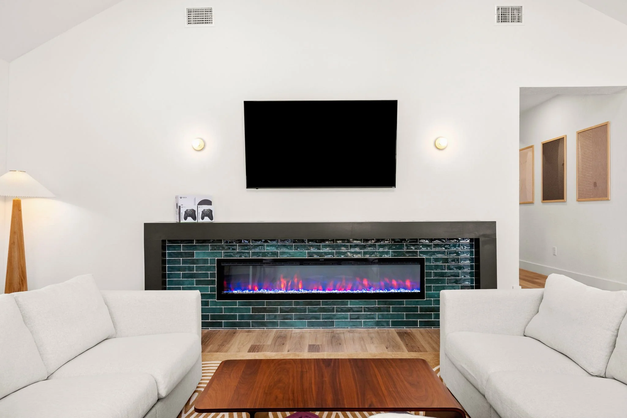 Living room with a fireplace, wall-mounted TV, two white sofas, wooden coffee table, and a lamp with a wooden stand.
