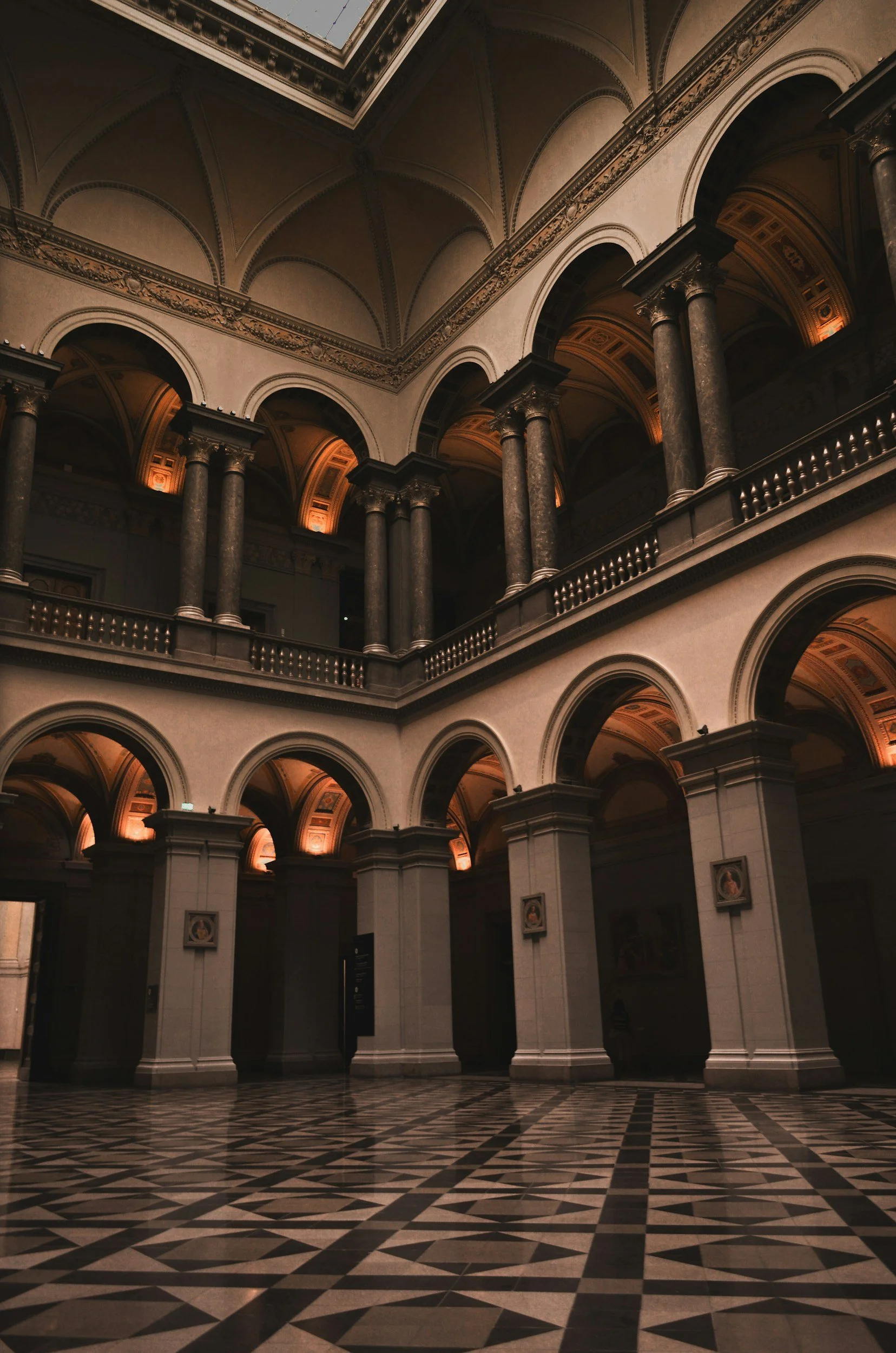 Interior of a grand historic building with tall columns, ornate arches, and a patterned black-and-white tiled floor.