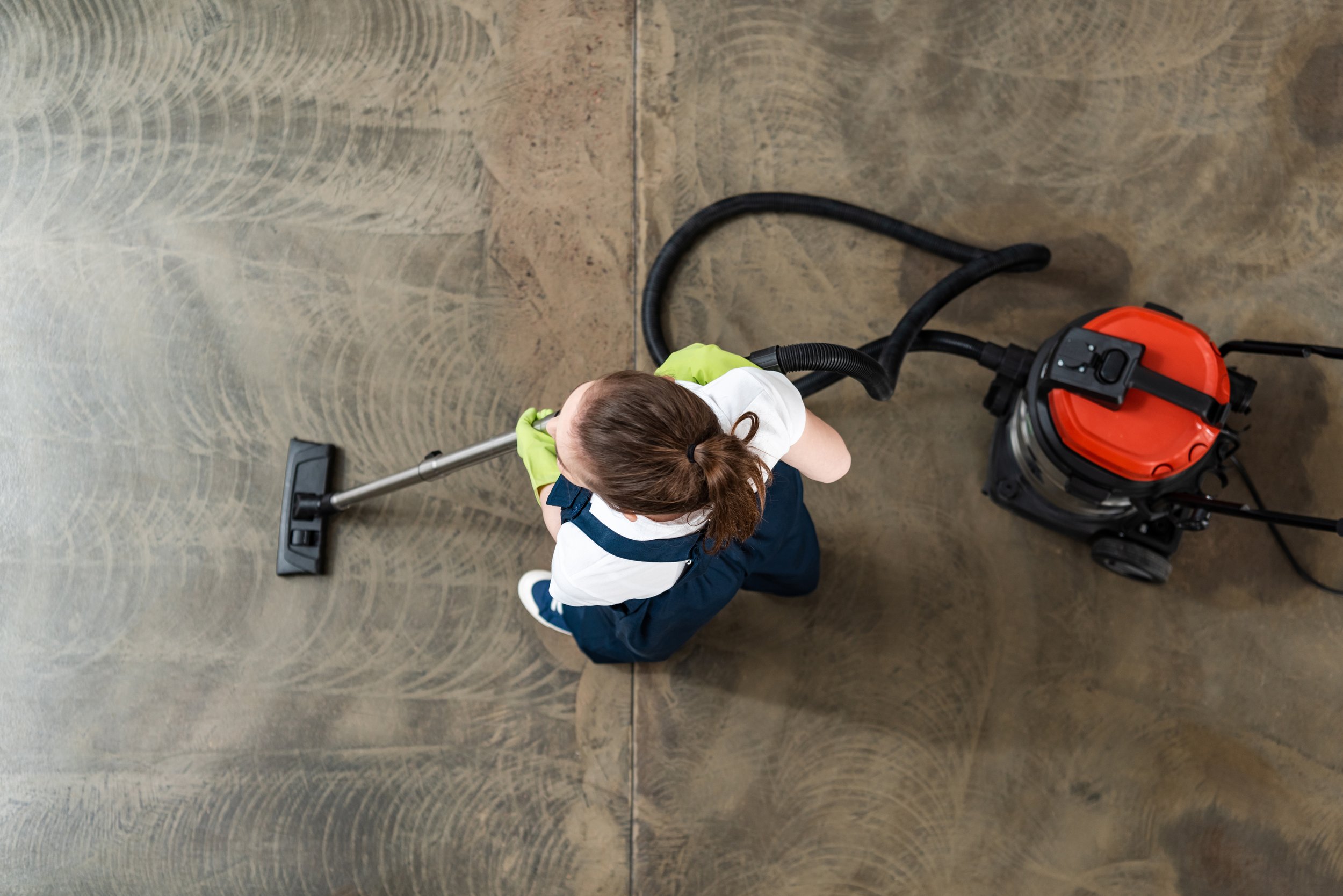 A woman wearing a white shirt and navy apron cleaning the floor with a vacuum cleaner.