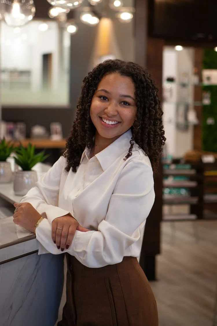 Camille est une jeune femme souriant devant la reception de la clinique d'audioprothèse