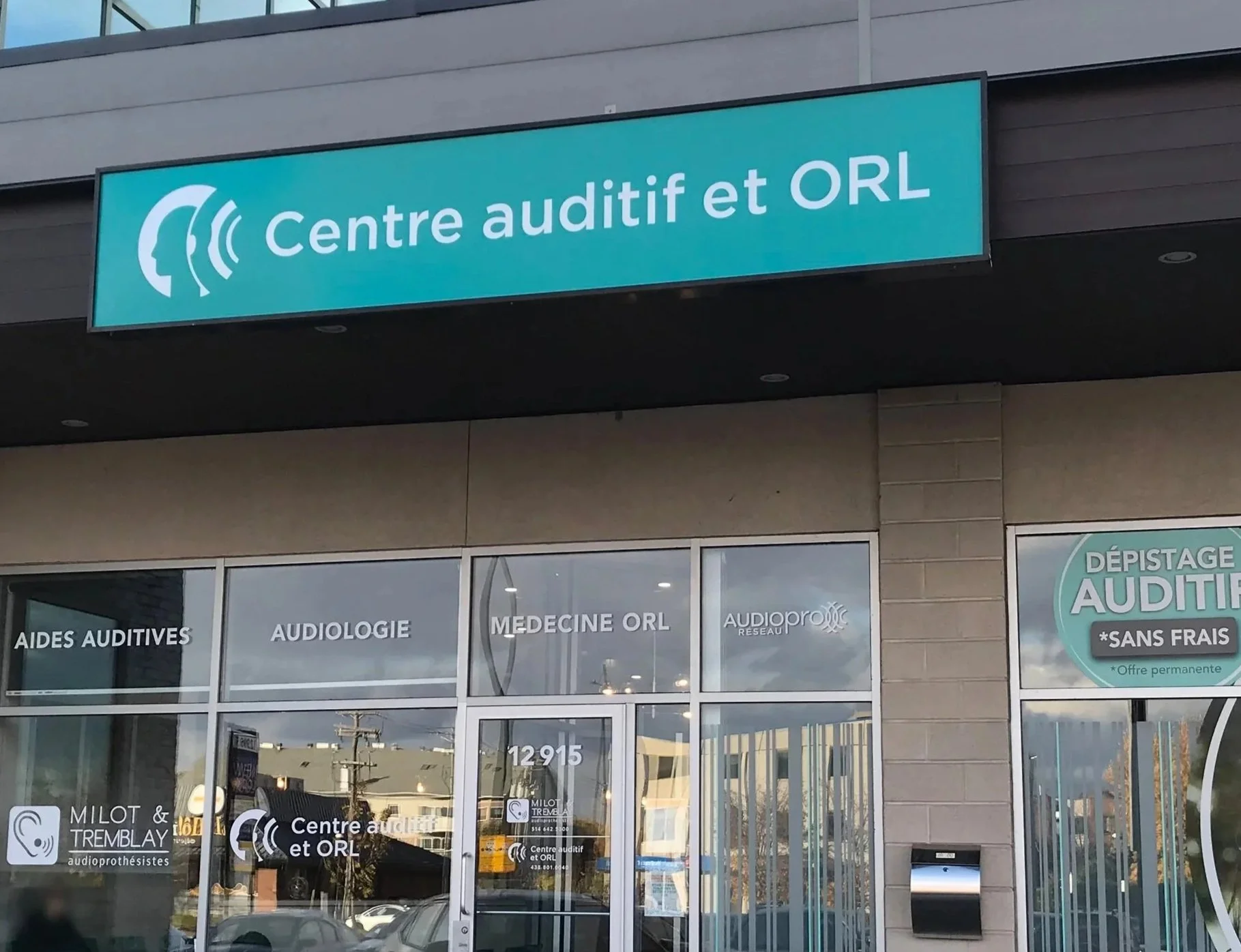 Façade d'un centre auditif avec un panneau bleu indiquant 'Centre auditif et ORL'. Vitrine avec inscriptions 'aides auditives', 'audiologie', 'médecine ORL' et 'réseau Audiopro'.