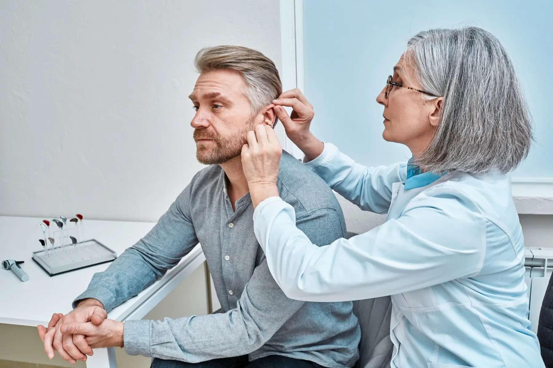 Une femme médecin examine un homme en lui insérant un petit appareil derrière l'oreille dans une clinique ou un hôpital.