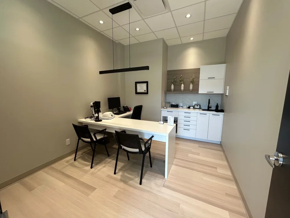 Bureau d'accueil avec un comptoir blanc, deux chaises, un ordinateur, une cafetière et un espace kitchenette avec des armoires blanches et des décorations