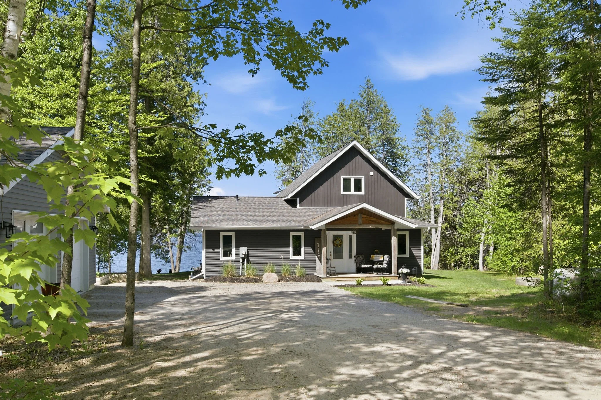 A gray house with a gray roof surrounded by green trees and a clear blue sky.