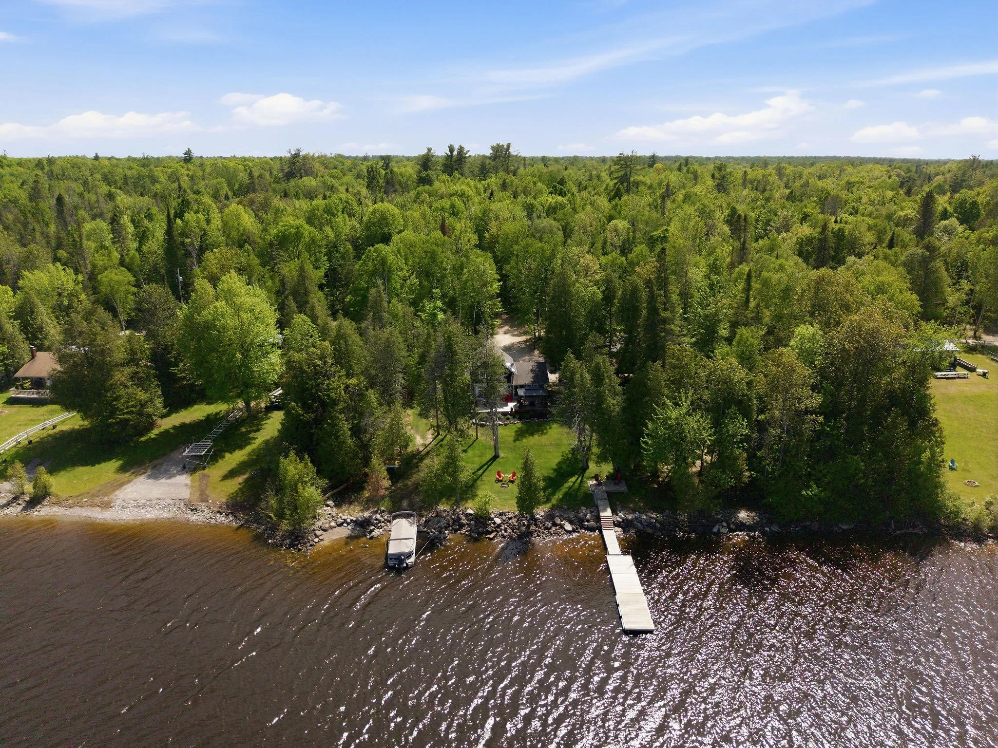 Aerial view of a lush green forest with a small boat dock extending into a river, with theable and houses along the shoreline in the distance.