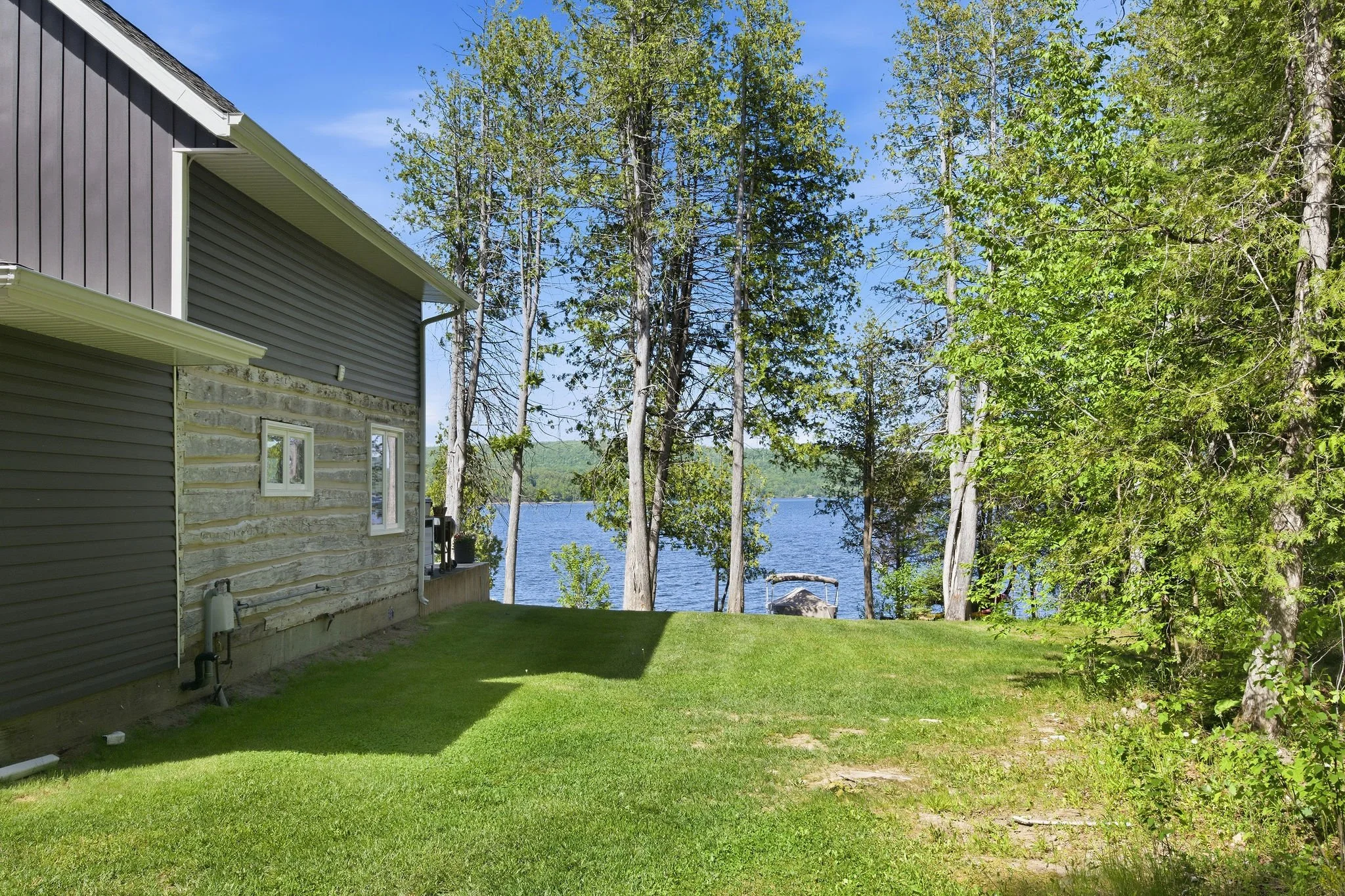 View of a backyard with green grass and trees near a lake, with part of a house visible on the left side.