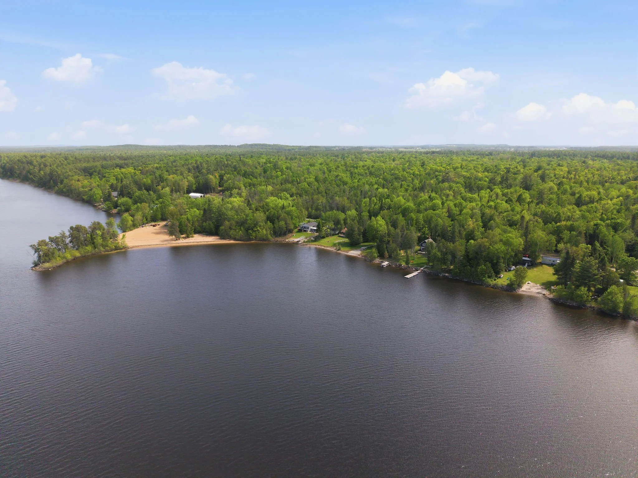 Aerial view of a lake surrounded by a dense forest with some houses and a small beach area.