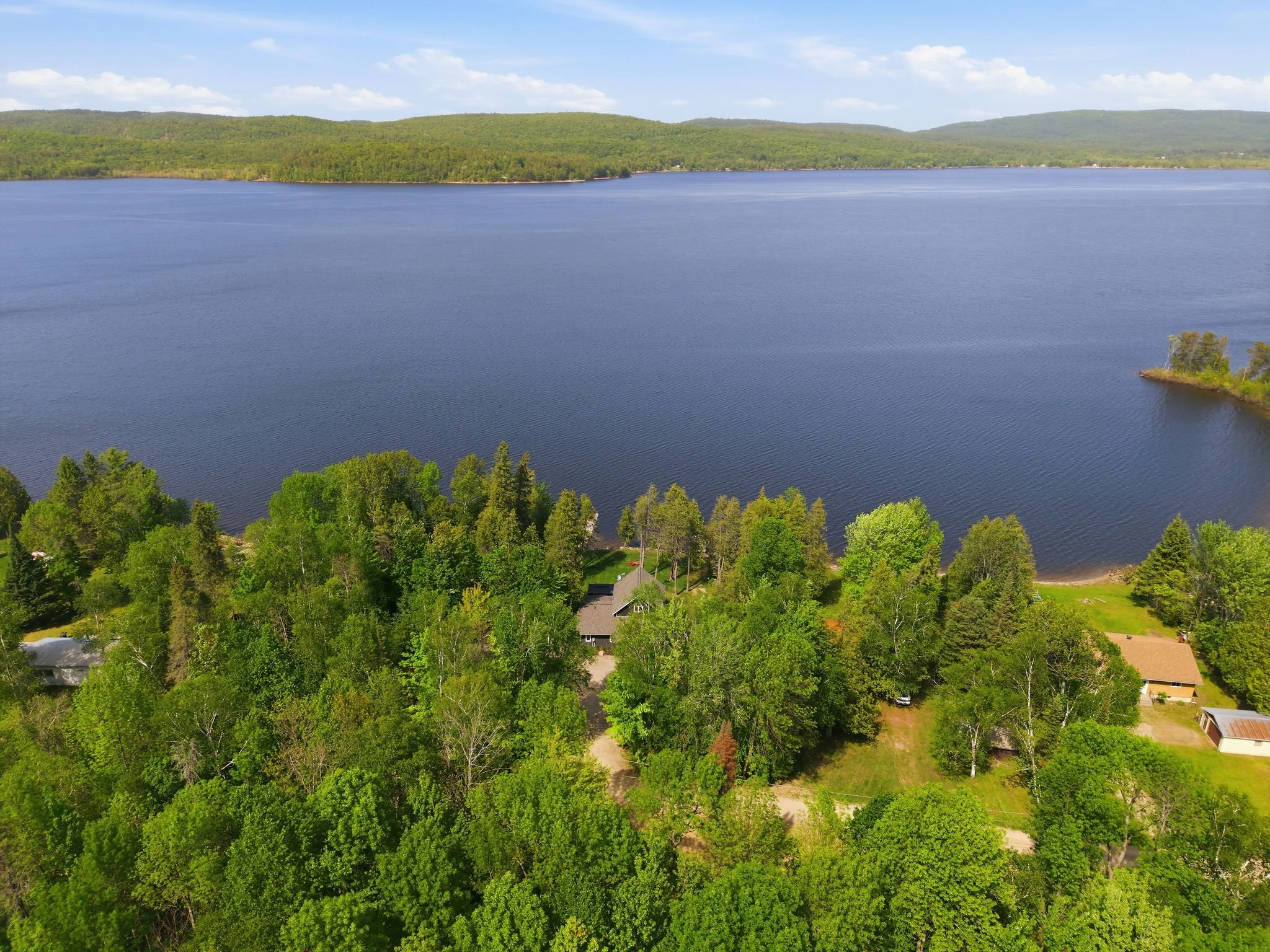 Aerial view of a large lake with green forested hills in the background and houses near the shoreline.