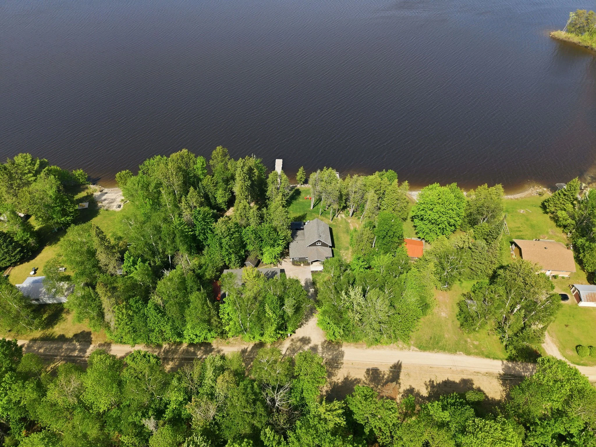 An aerial view of a residential neighborhood with lush green trees, houses, and a road, next to a large body of water, possibly a lake or river.