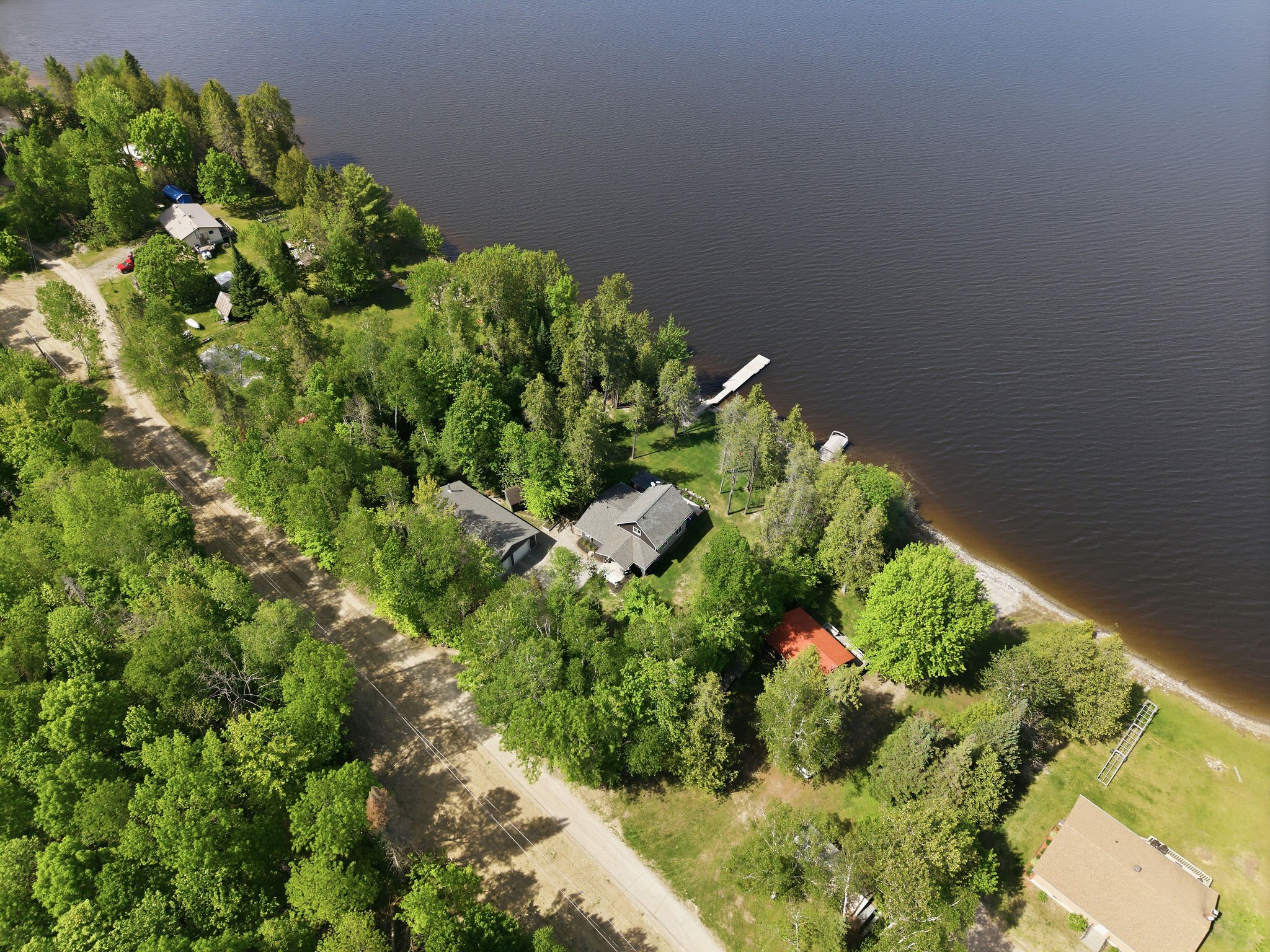 Aerial view of a lakeside residential area with houses, trees, and a wooden dock extending into the lake.