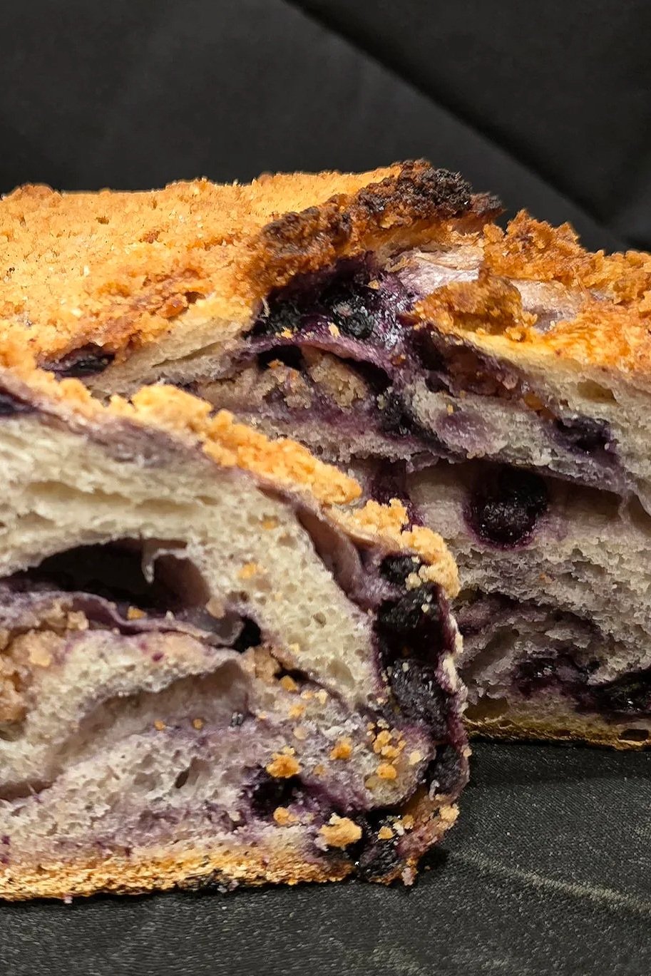 Close-up of a slice of blueberry bread with blueberries and a crumbly top.
