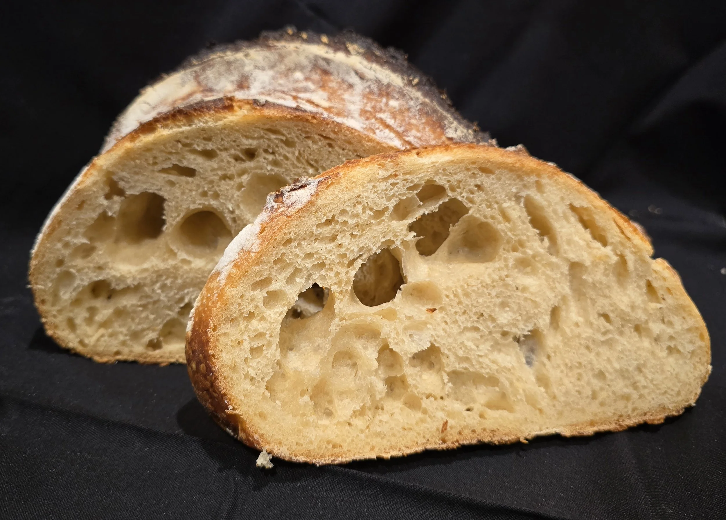 Two slices of classic sourdough bread with a crusty exterior and airy interior, resting on a black surface.