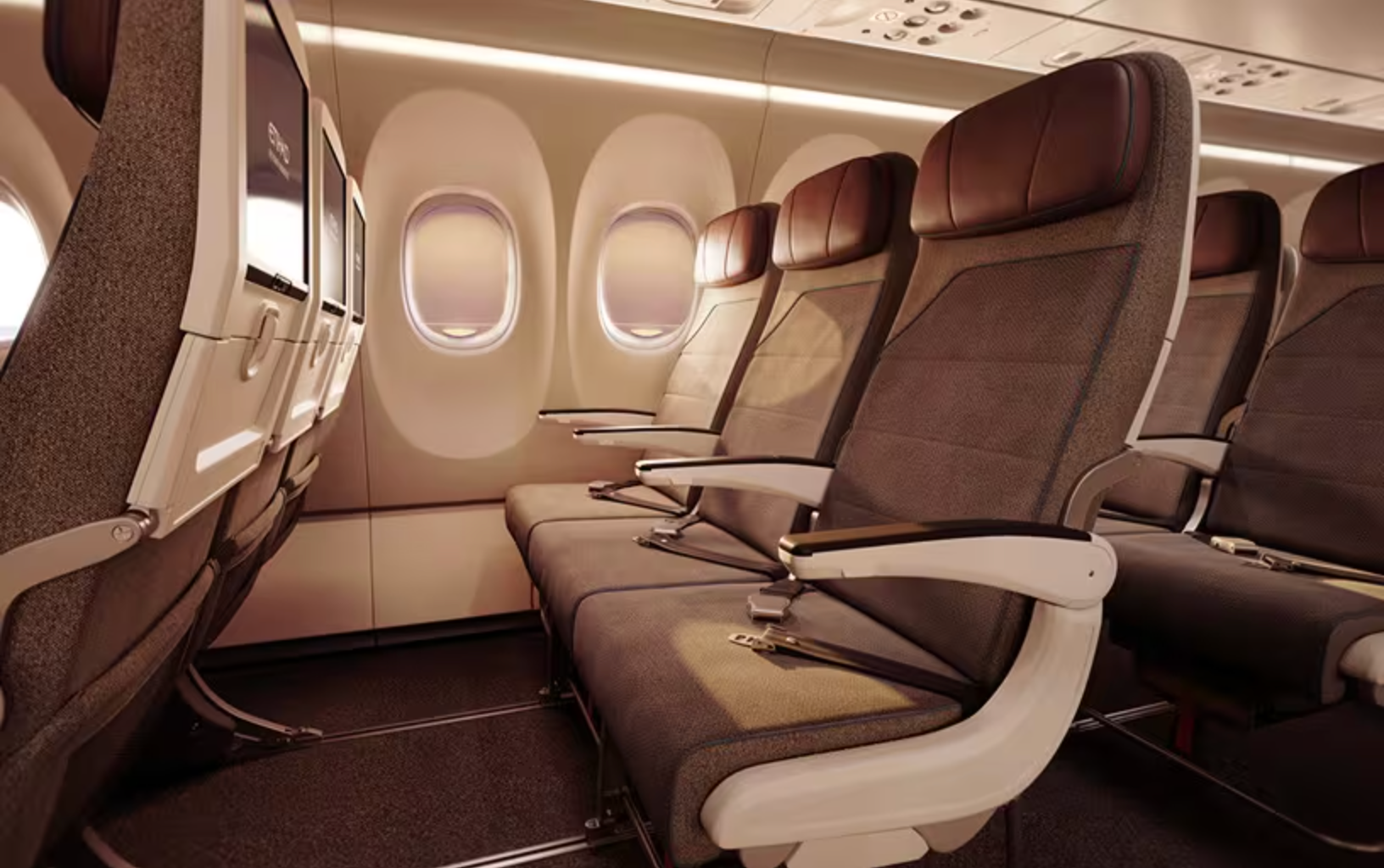 Empty airplane cabin with three water in seat rows, gray fabric seats, and in-flight entertainment screens.
