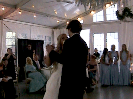A bride and groom dance at their wedding reception with guests watching.