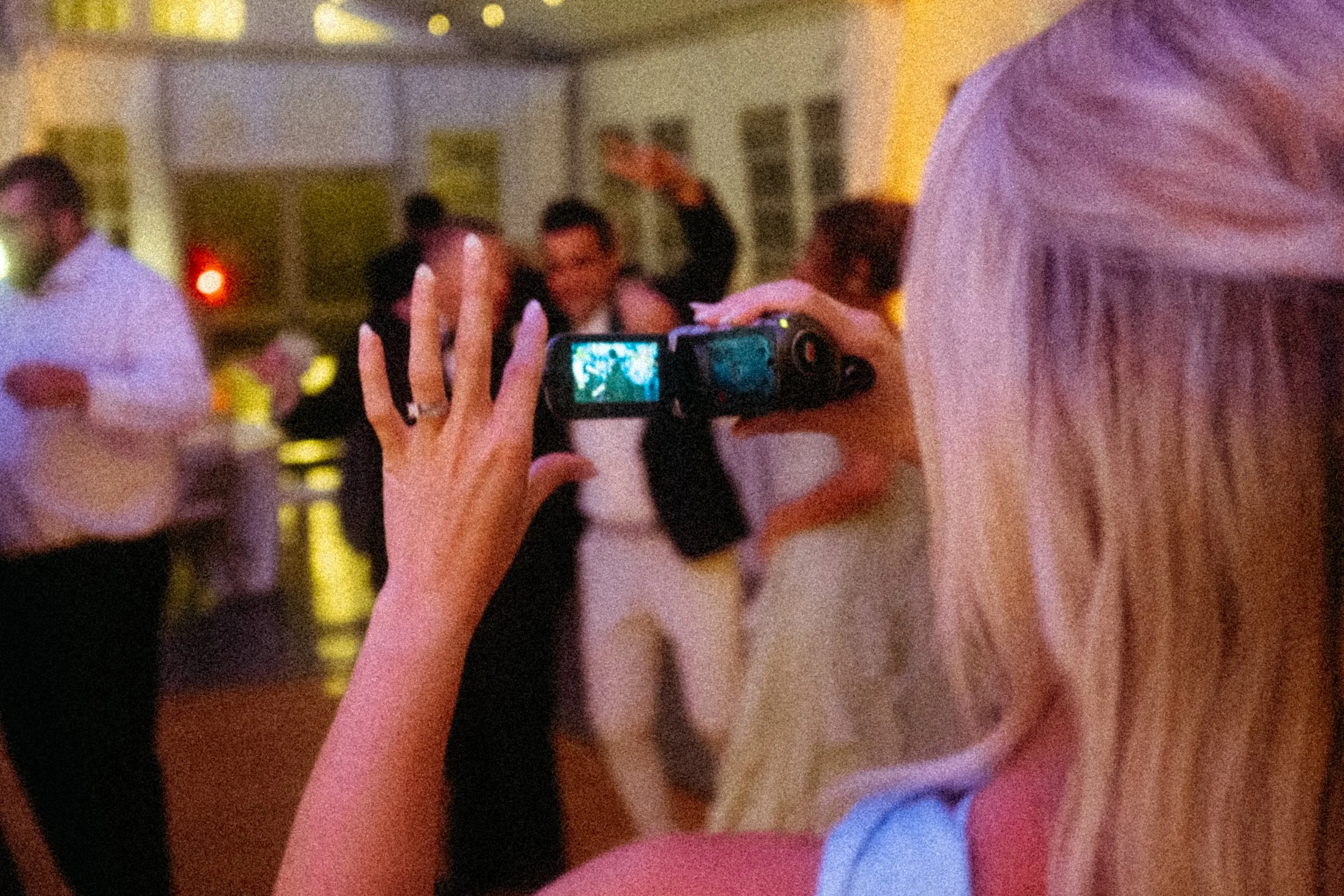 A bridesmaid is filming a wedding dance floor using an old camcorder