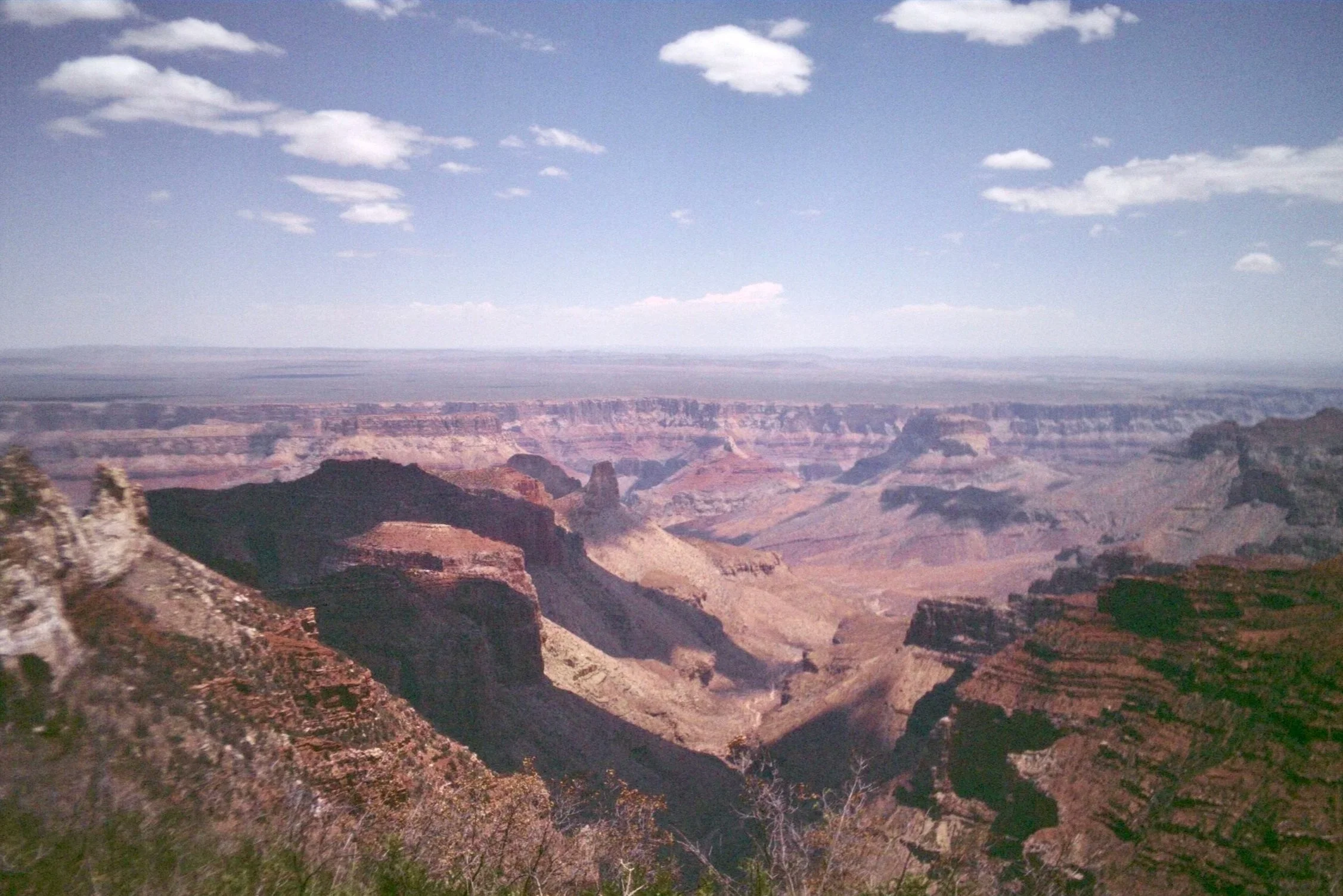 Scenic view of the Grand Canyon with layered rock formations, cliffs, and a cloudy sky. Taken on a disposable camera to give a nostalgic, vintage look.