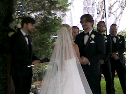 Bride and groom exchanging vows during outdoor wedding ceremony, with witnesses standing nearby.