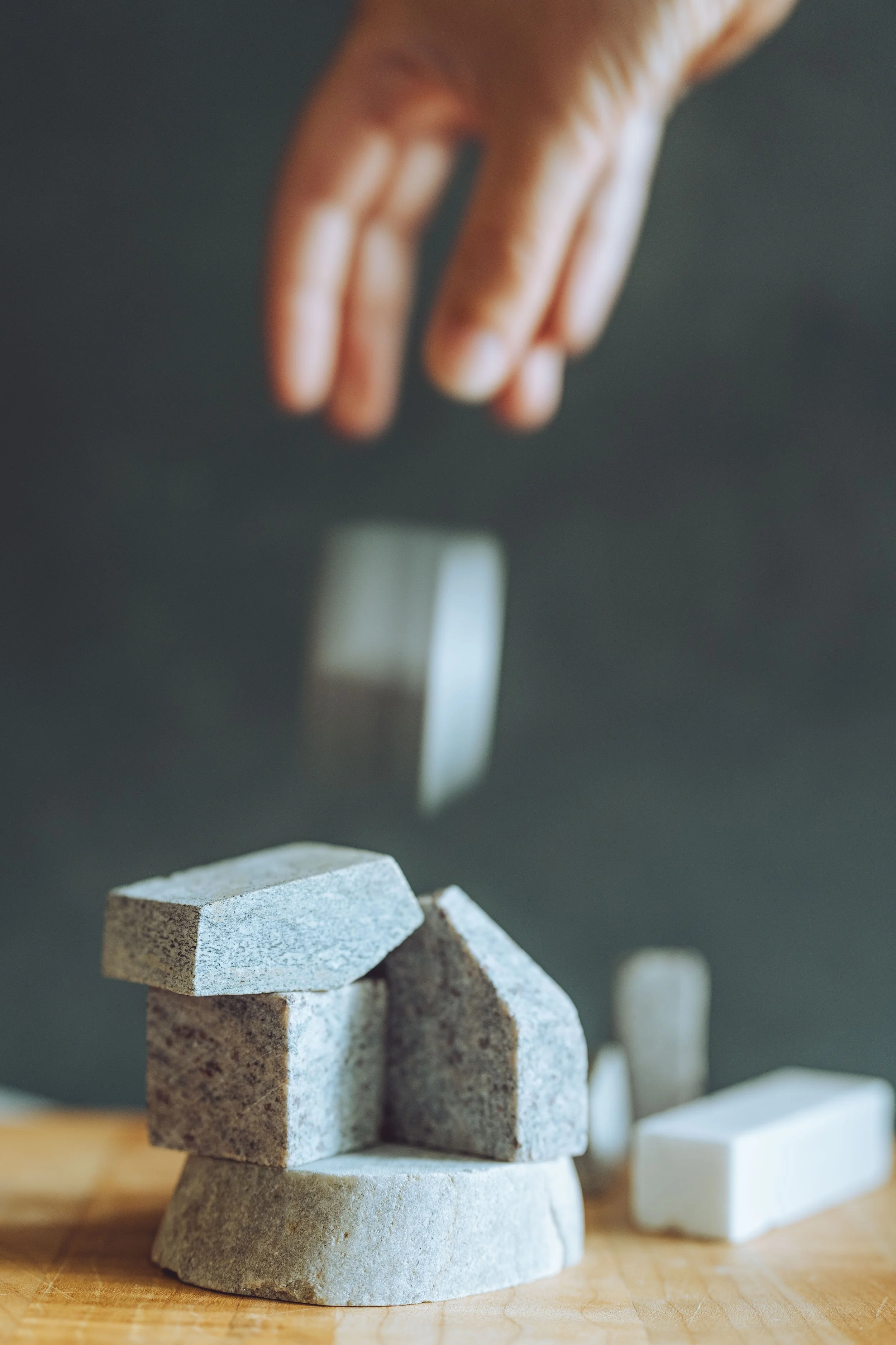 A hand dropping a rectangular stone block onto a stack of similar stones, balancing it in a game of agility and precision on a wooden surface with other stones nearby.