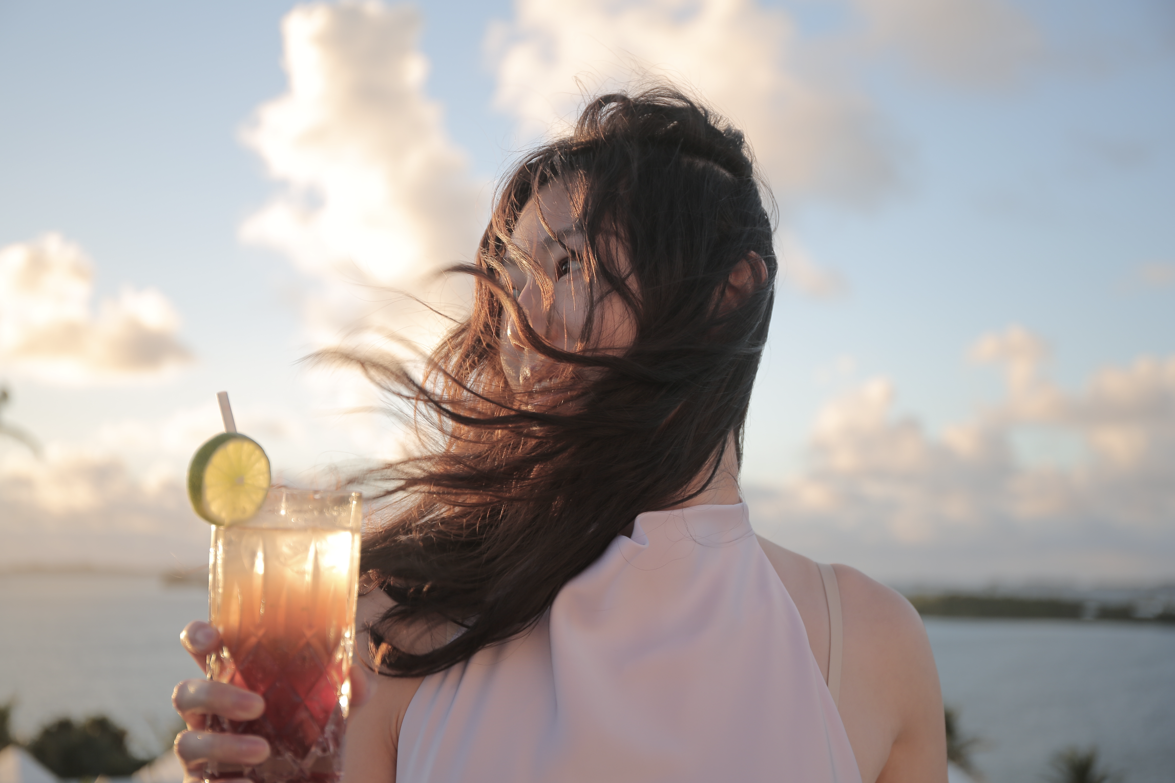 Cinematic lifestyle portrait of a woman holding a colorful layered drink at sunset, natural outdoor light and soft sky, photography by Jing Xiao