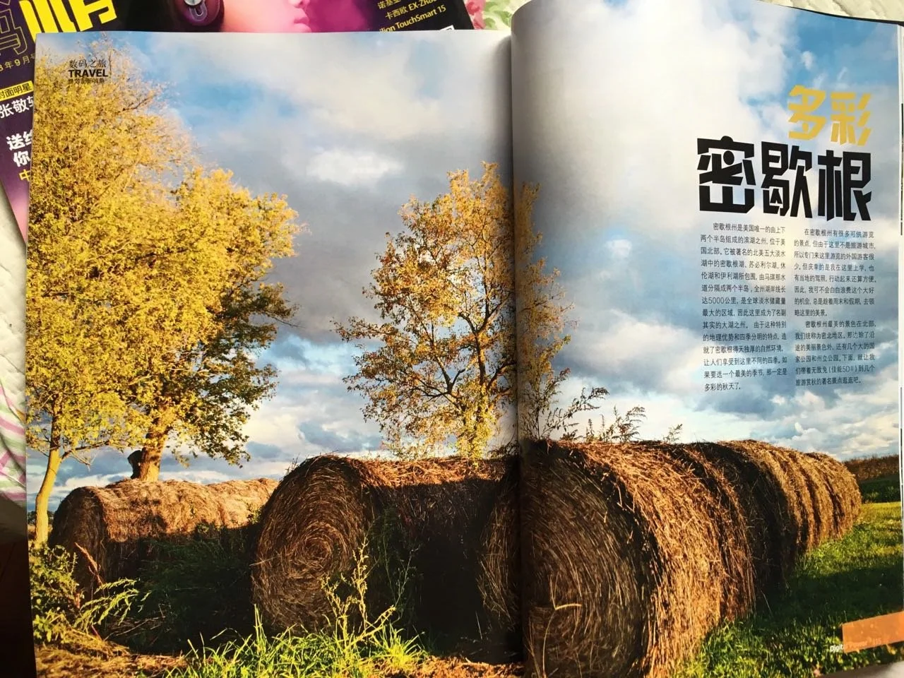 Open magazine with a two-page spread showing a rural scene of hay bales, trees with yellow leaves, a partly cloudy sky, and some green grass.