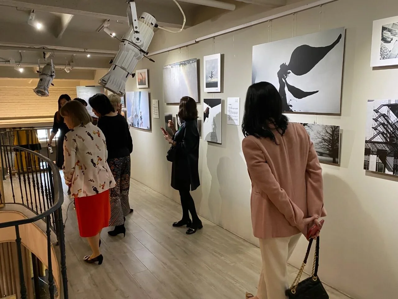 People viewing artwork in an art gallery, with black and white photographs and art pieces hanging on the wall.