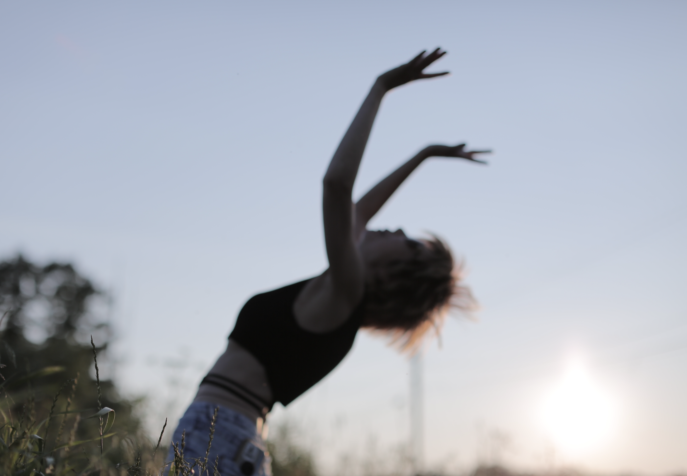 Cinematic lifestyle portrait of a person with raised arms and flowing hair in an outdoor natural setting at golden hour, surrounded by trees, expressive movement and warm light, photography by Jing Xiao