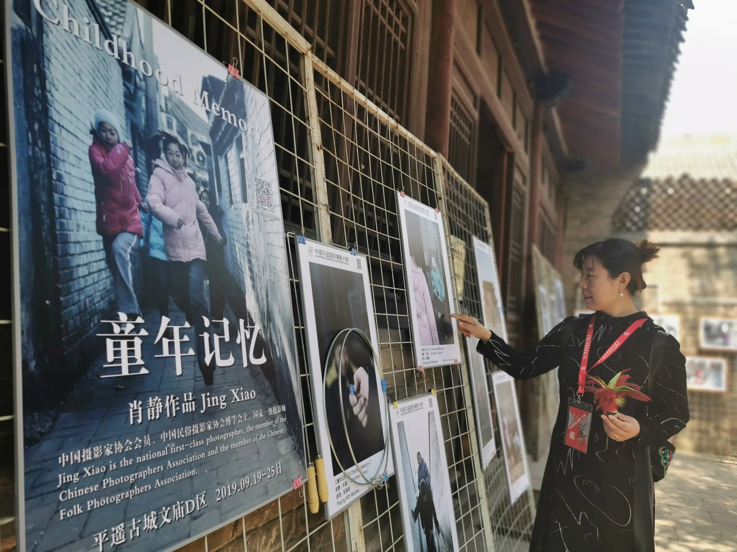 A woman looking at a display of photographs and posters at an outdoor exhibition, with traditional wooden building in the background.