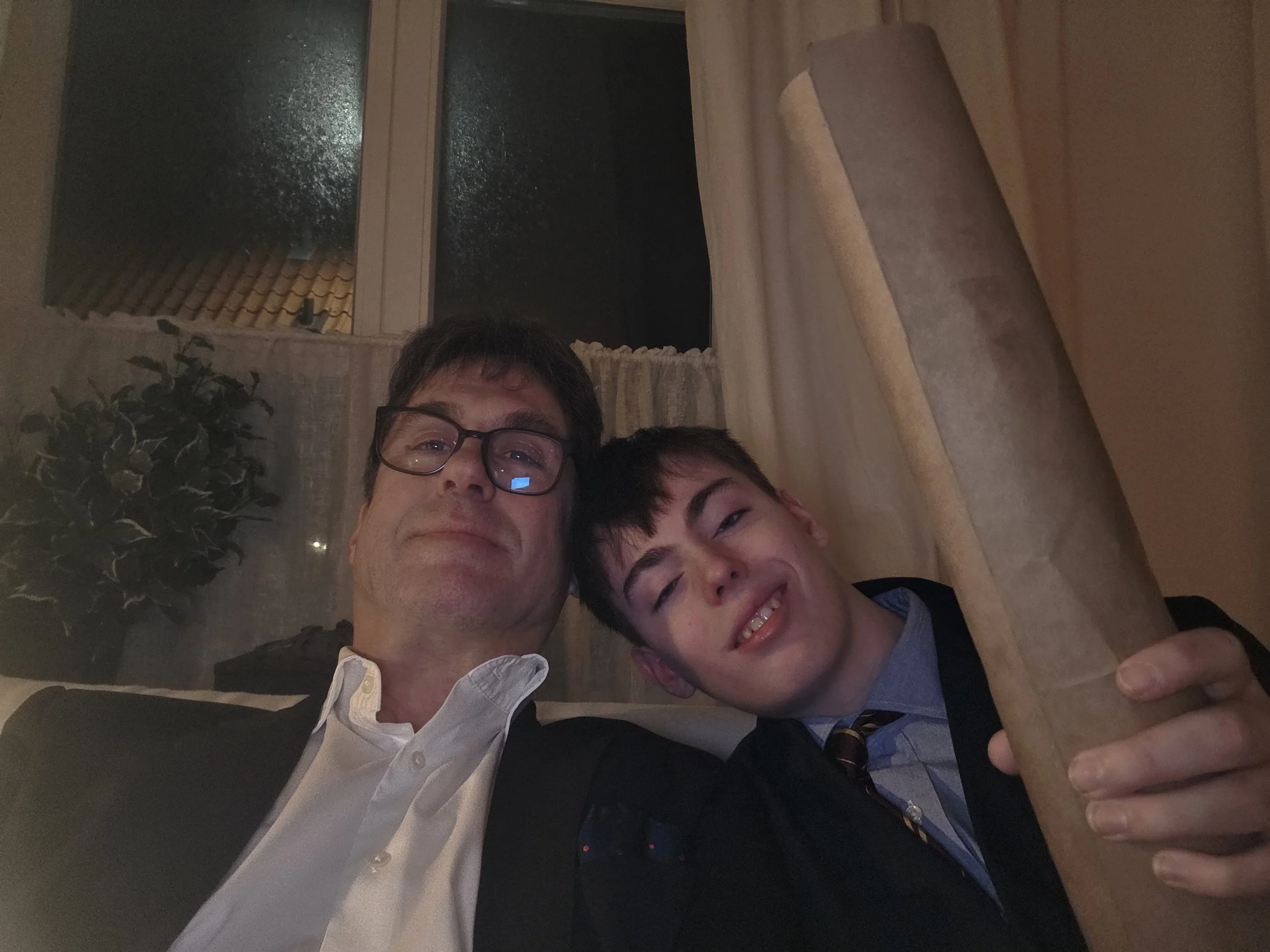 A father and son taking a selfie together in a cozy indoor setting at night.