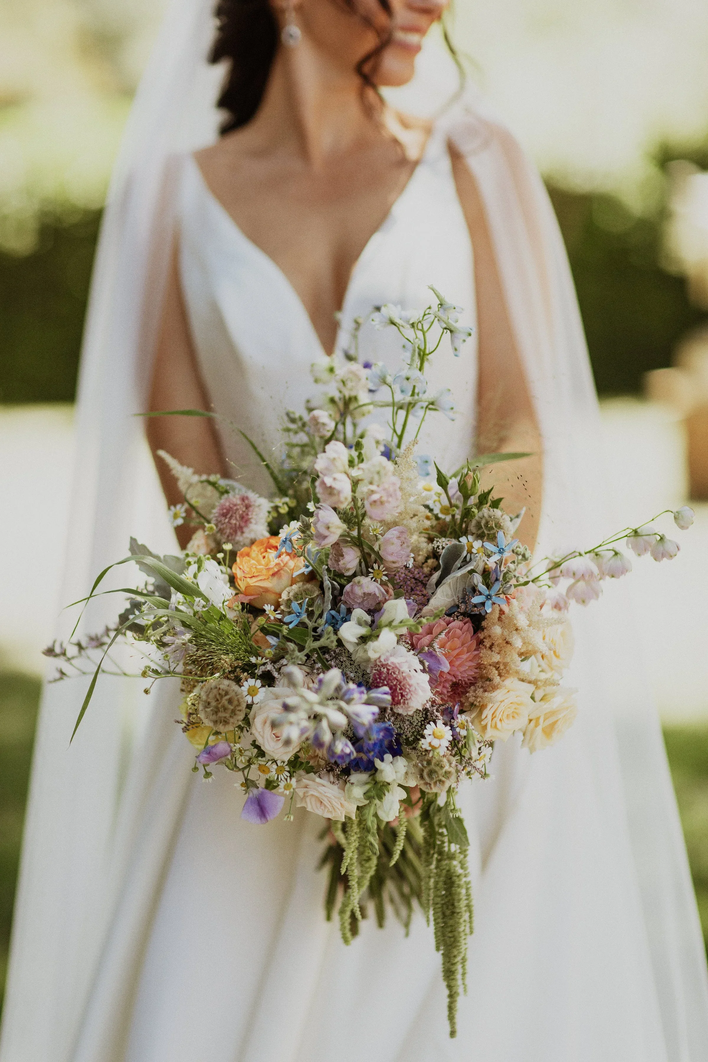 Close-up of a bride holding a colorful bouquet of flowers, with a blurred outdoor background. Example of what your wedding bouquet could look like at Grand Shores.
