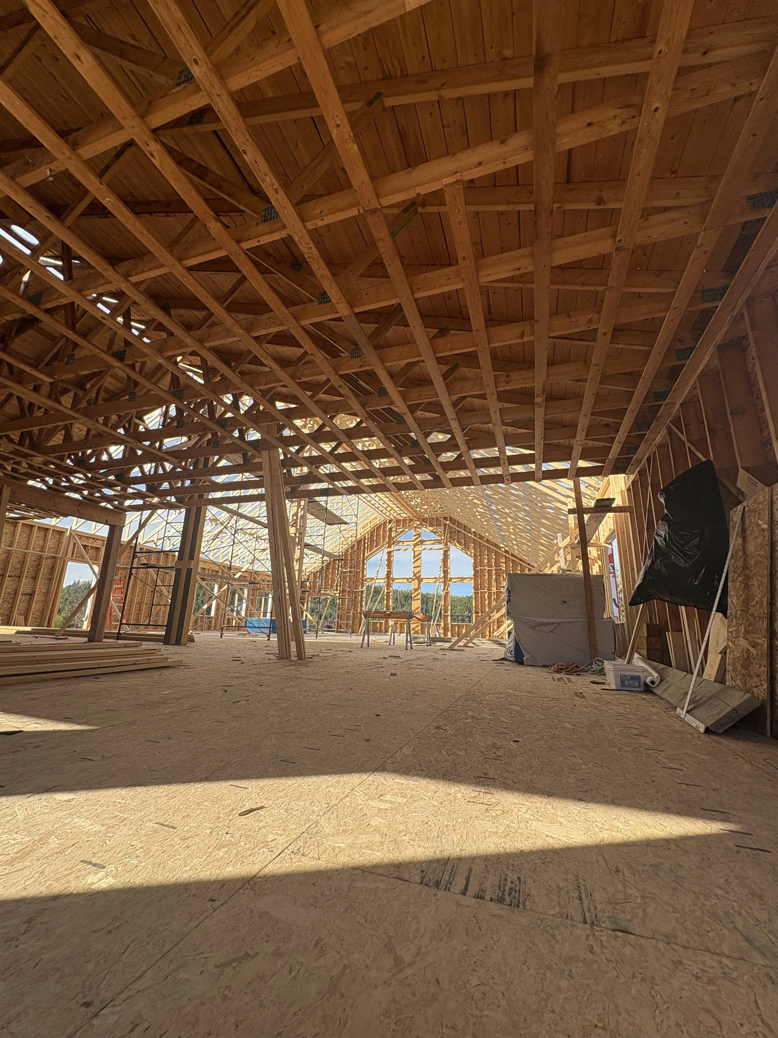 Interior of the Grand Shores wedding venue under construction with exposed wooden framing and roof trusses, construction materials and tools scattered on the floor.