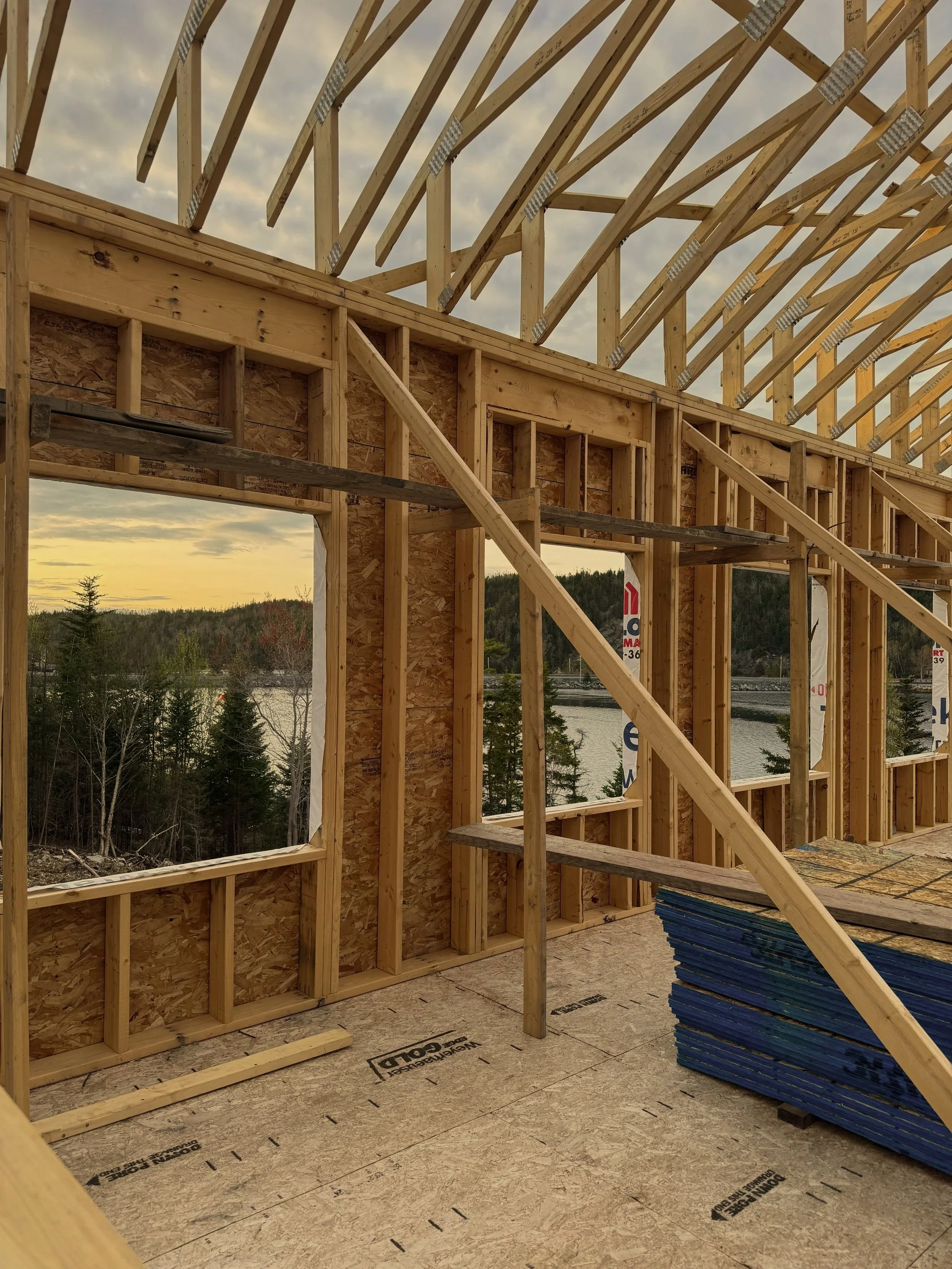 Wood framing of a the Grand Shores event building under construction, with unfinished walls and roof supports, view of landscape with trees and sky in the background.
