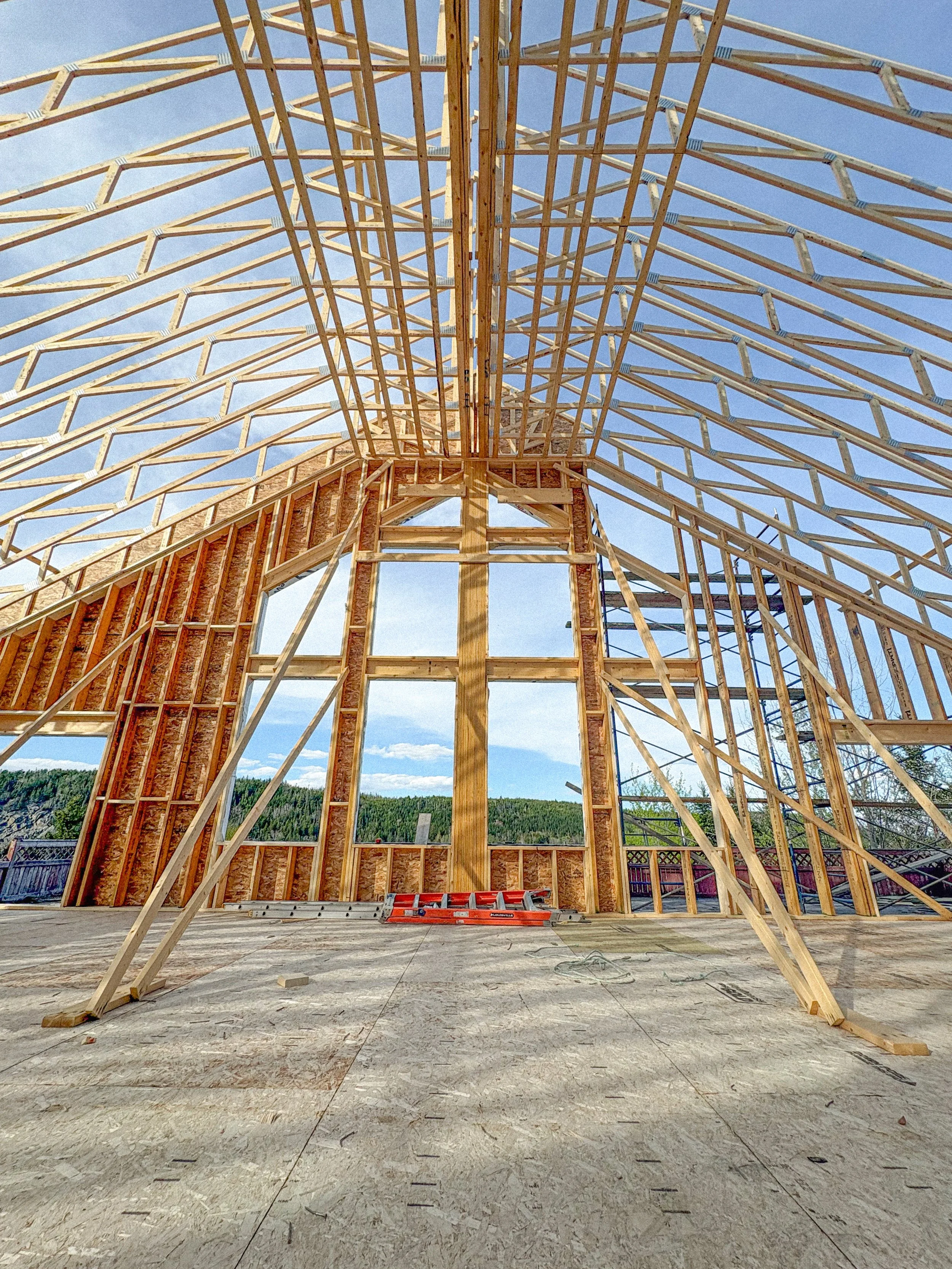 Wooden framing of a wedding venue under construction on the Eastern Shore of Nova Scotia, with a clear blue sky and distant trees in the background.