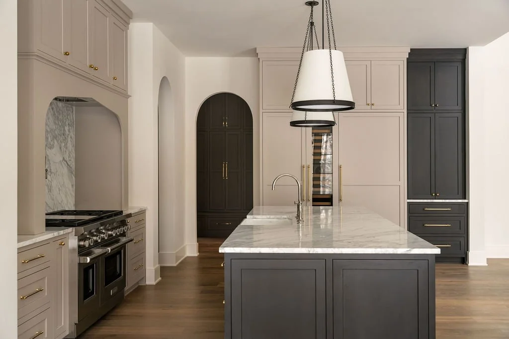 Modern kitchen with white and dark navy cabinets, marble countertop island, stainless steel stove, and hanging pendant lights.