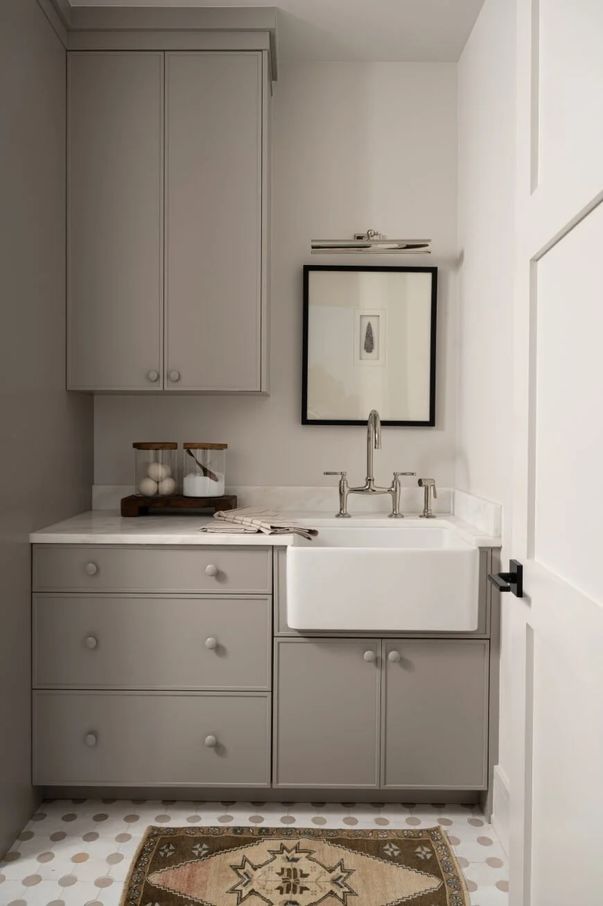 Farmhouse sink, polished nickel fixtures, and soft patterned tile layered with warm gray cabinetry for a clean, timeless laundry room.