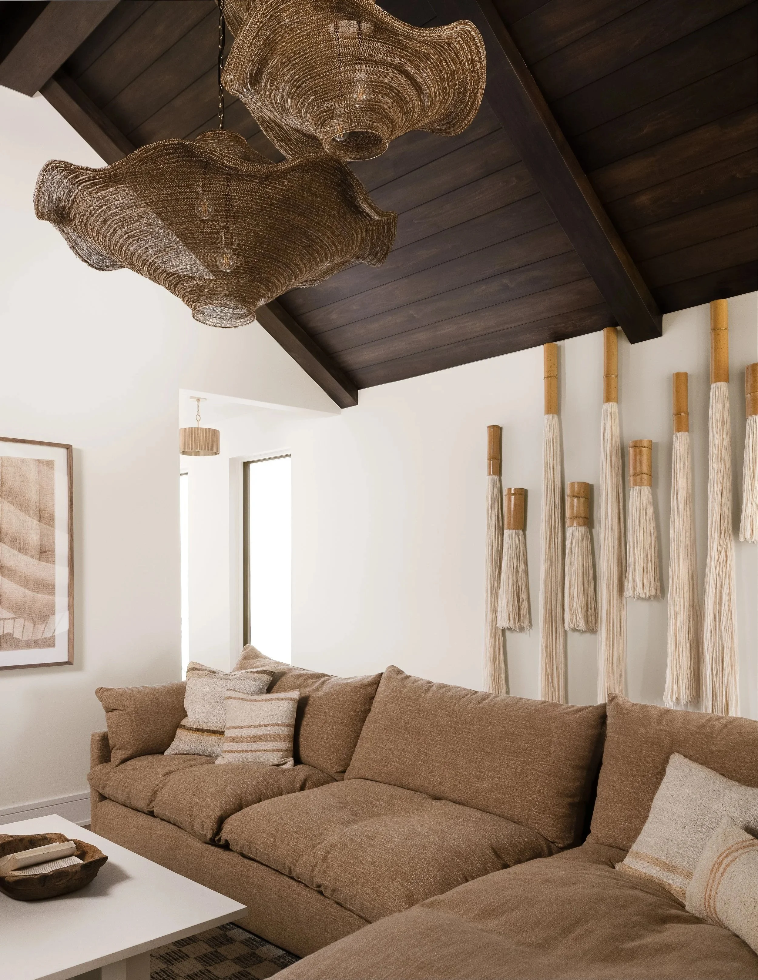 A lounge with dark wood paneled ceiling and oversized woven pendant lights.